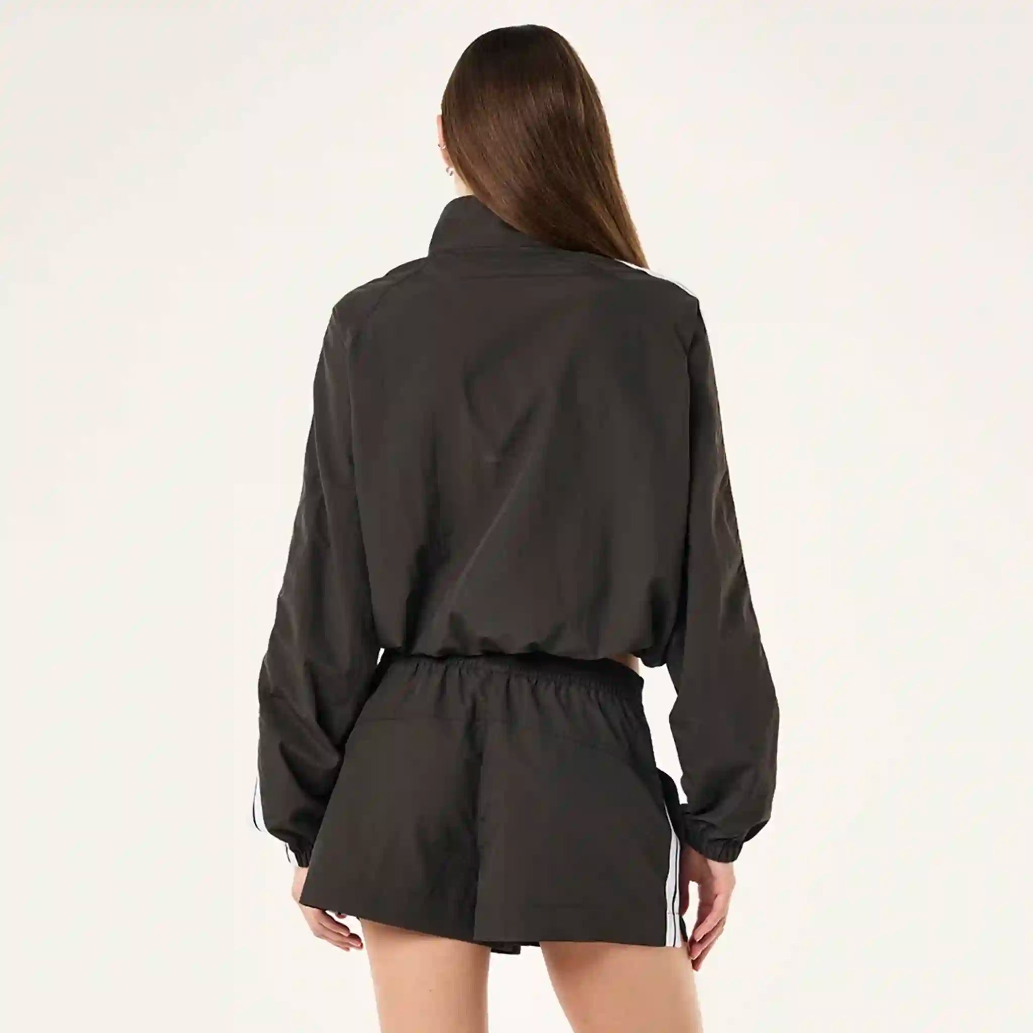 Person wearing a black jacket and shorts with white stripes on a light gray background