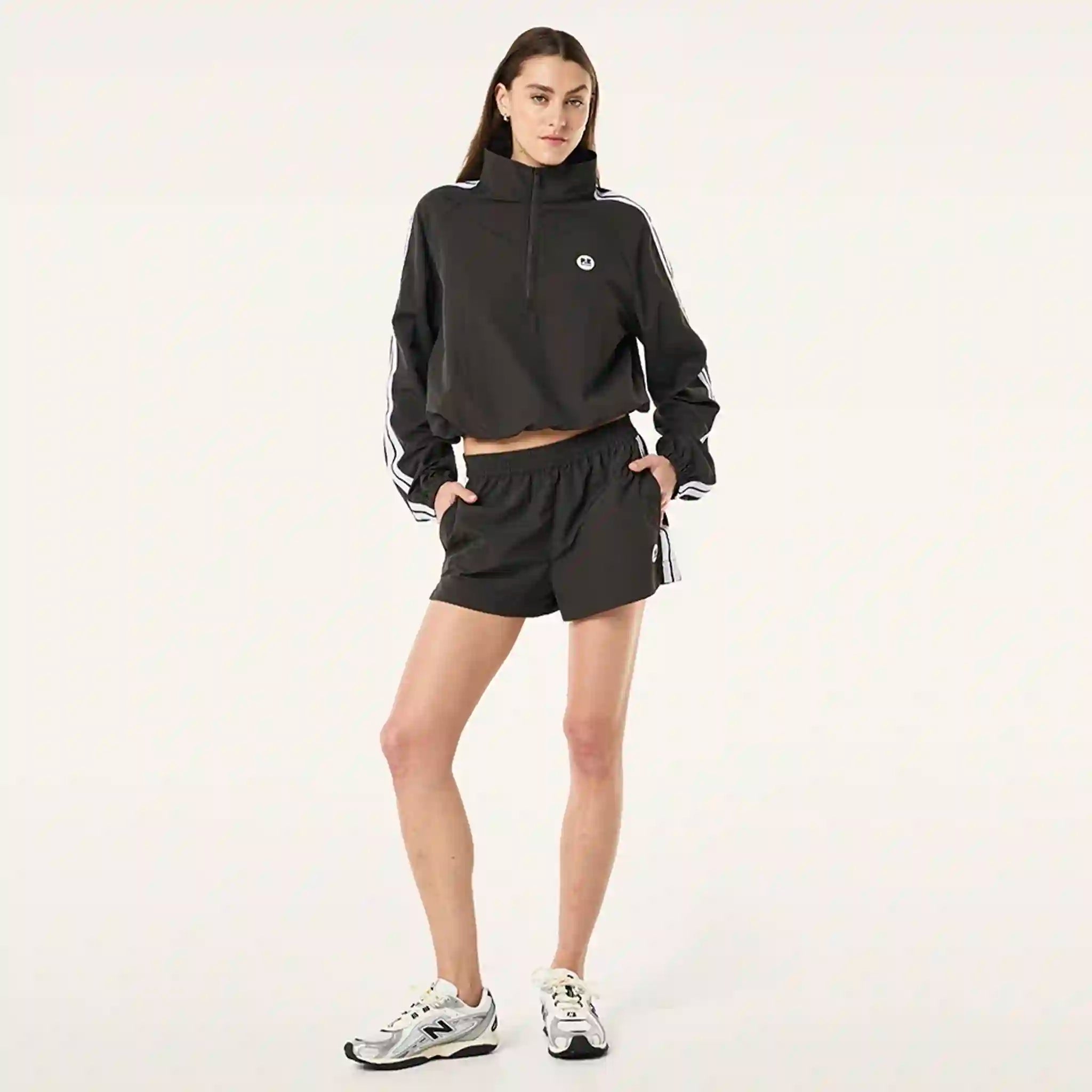 Person wearing a black jacket and shorts with white stripes on a light gray background