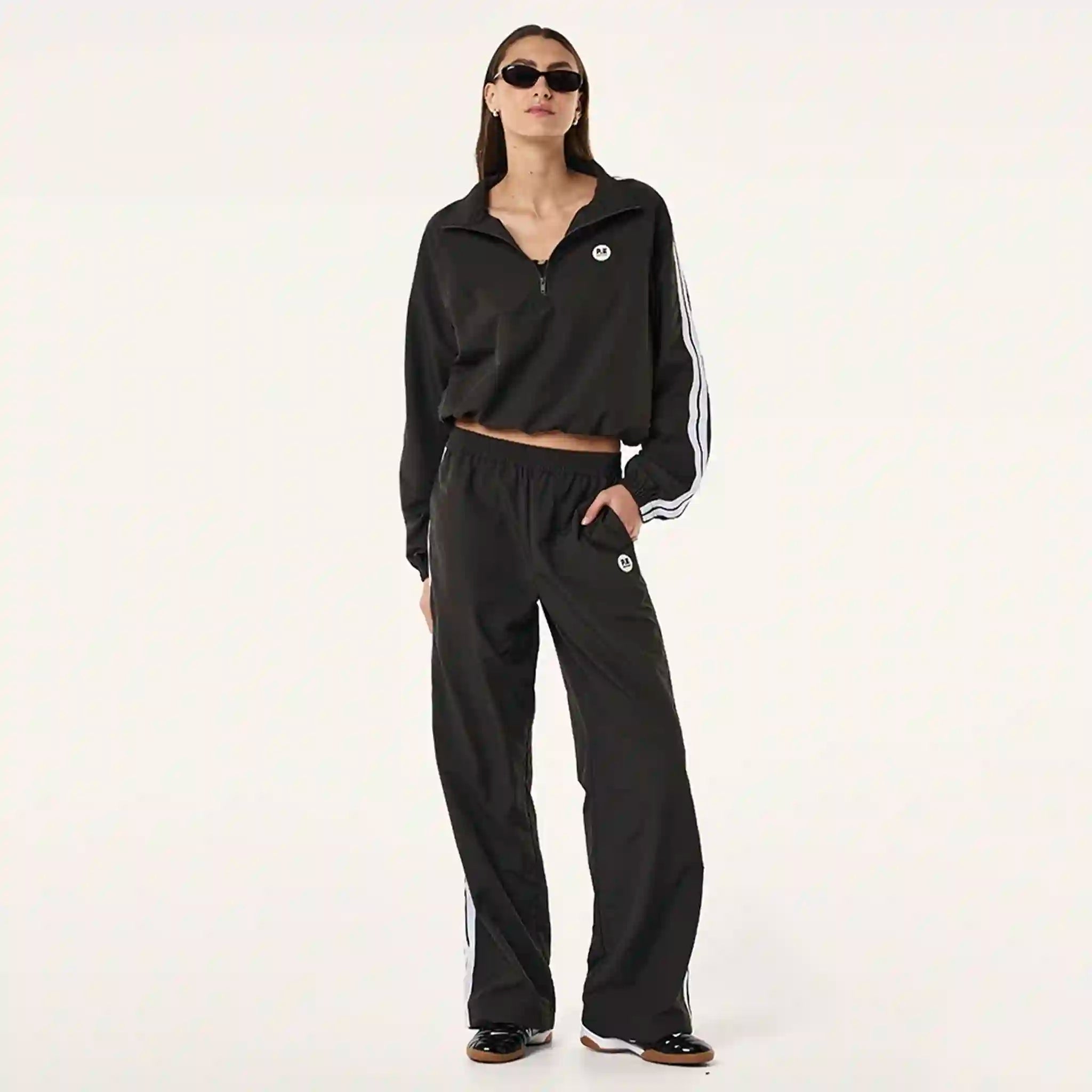 Person wearing a black jacket and pants with white stripes on a light gray background