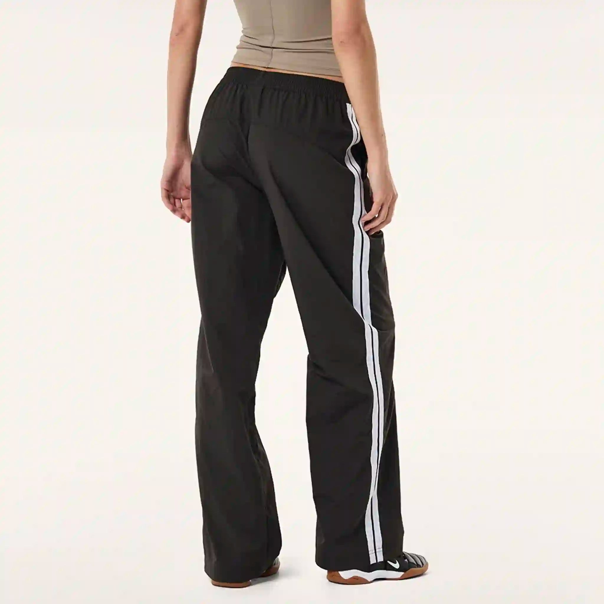 Black track pants with white stripes on a plain background