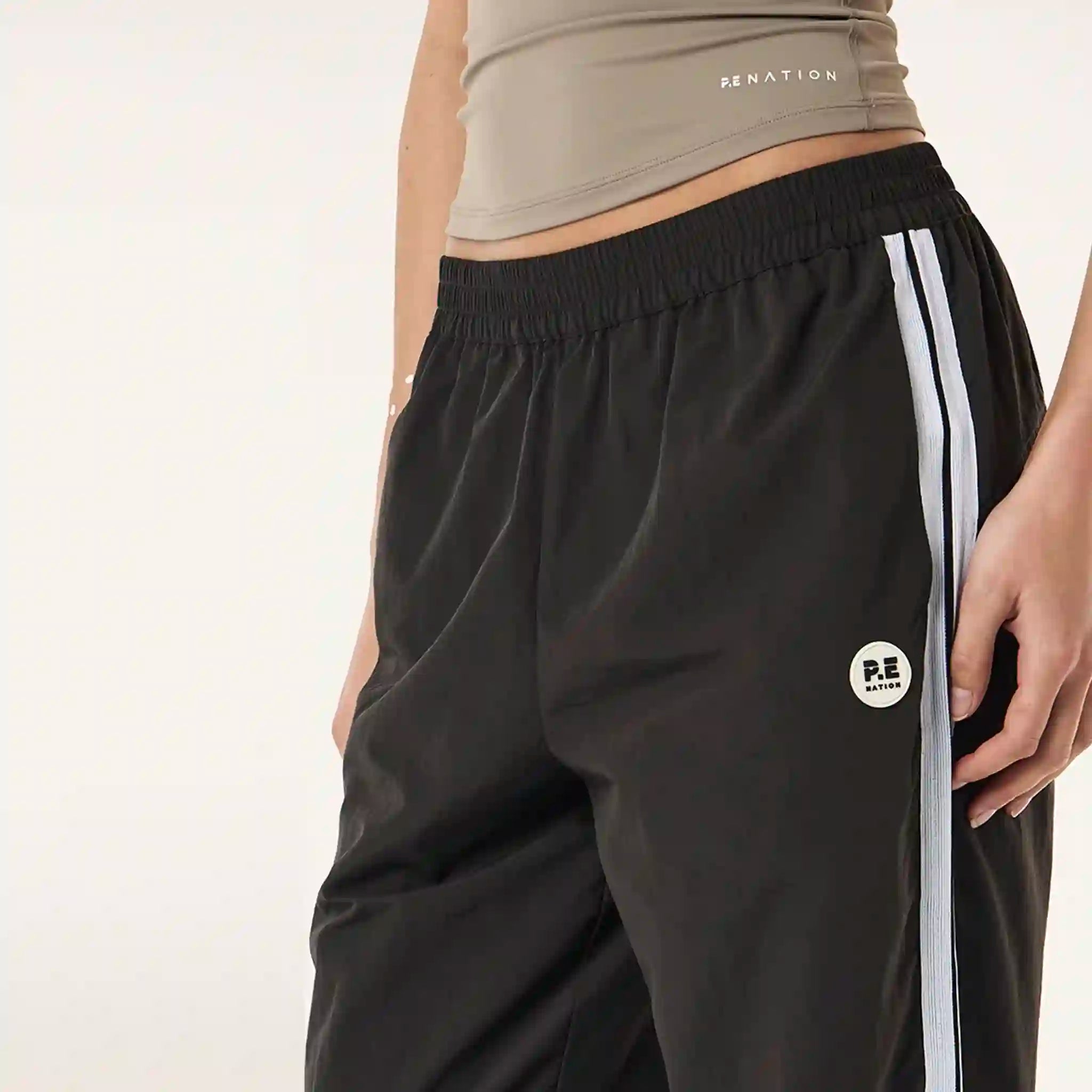 Black athletic pants with white stripes and a logo on a plain background