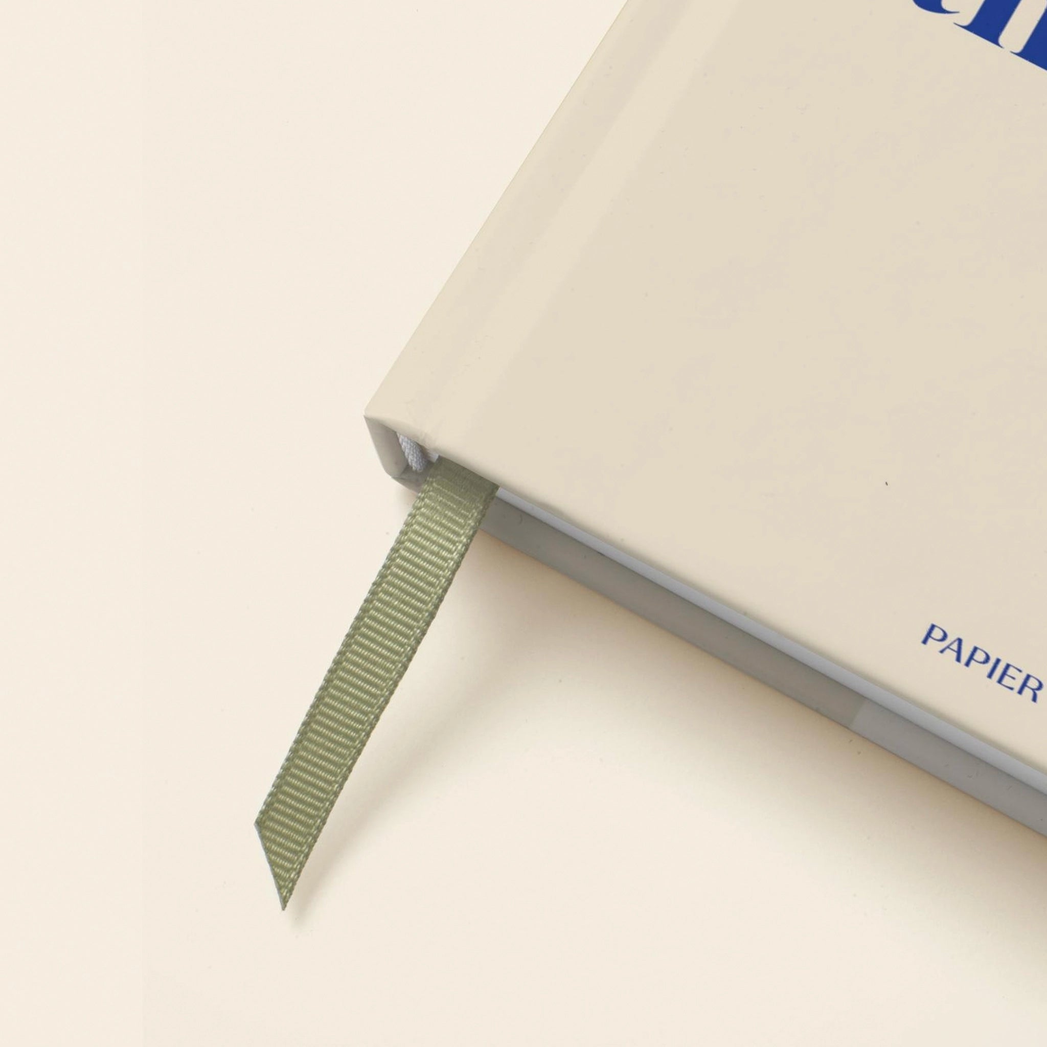 Close-up of a notebook with a green ribbon bookmark on a beige background