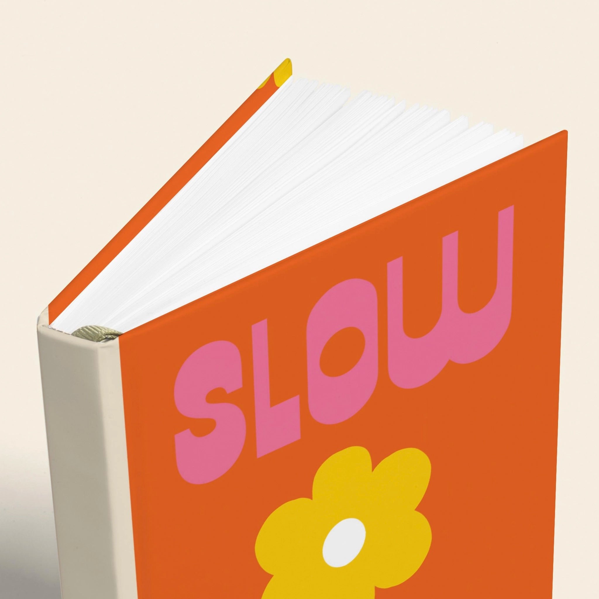 Book with 'SLOW' in pink and a flower on an orange cover against a beige background