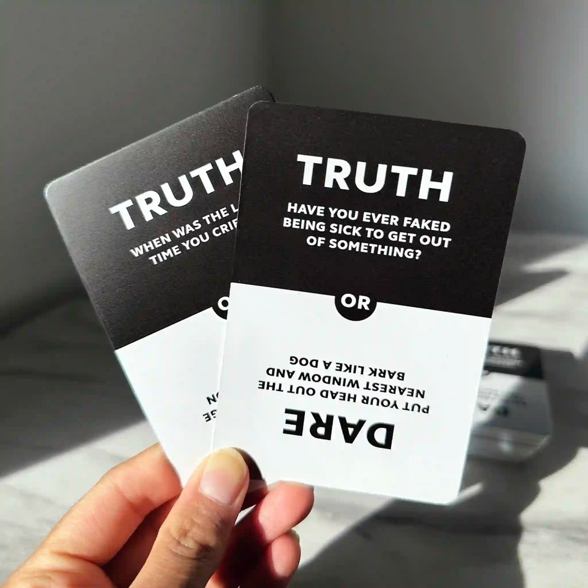 Hand holding truth or dare cards with text on a neutral background