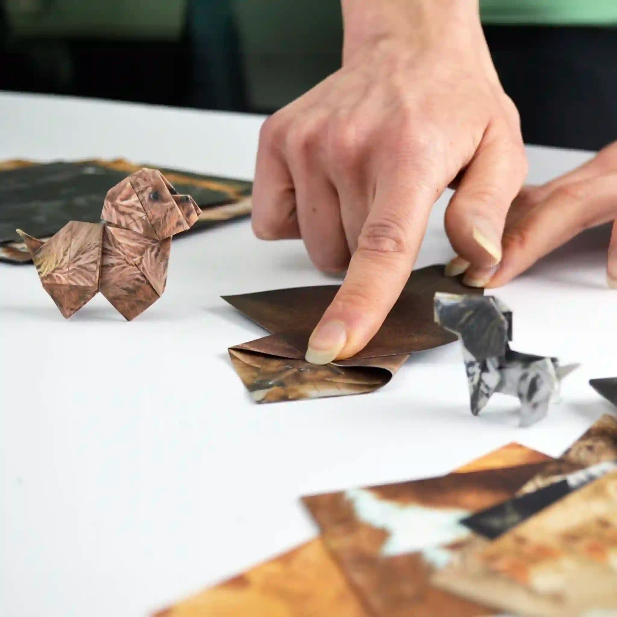 Hand arranging origami animals on a white surface