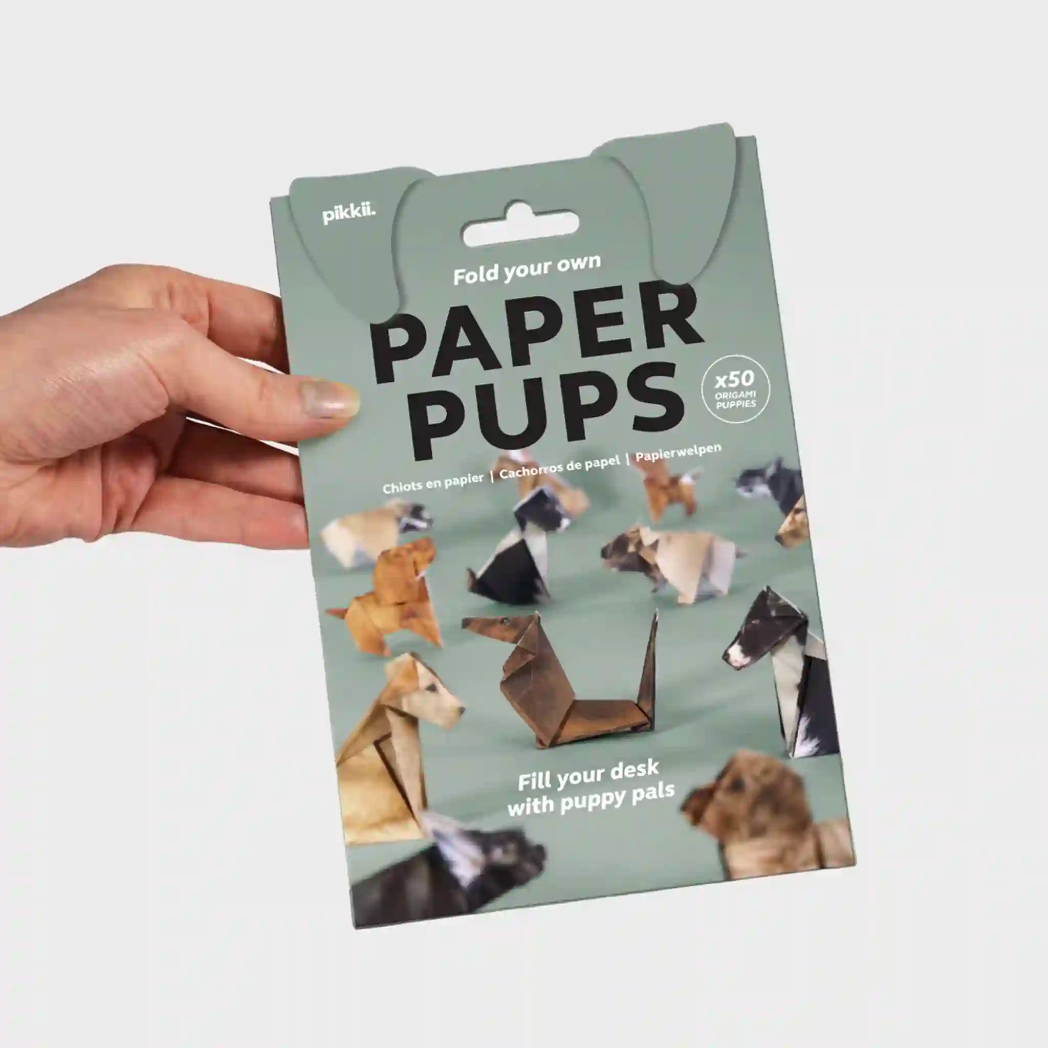 Packaging of paper dog models with a hand holding it on a light gray background