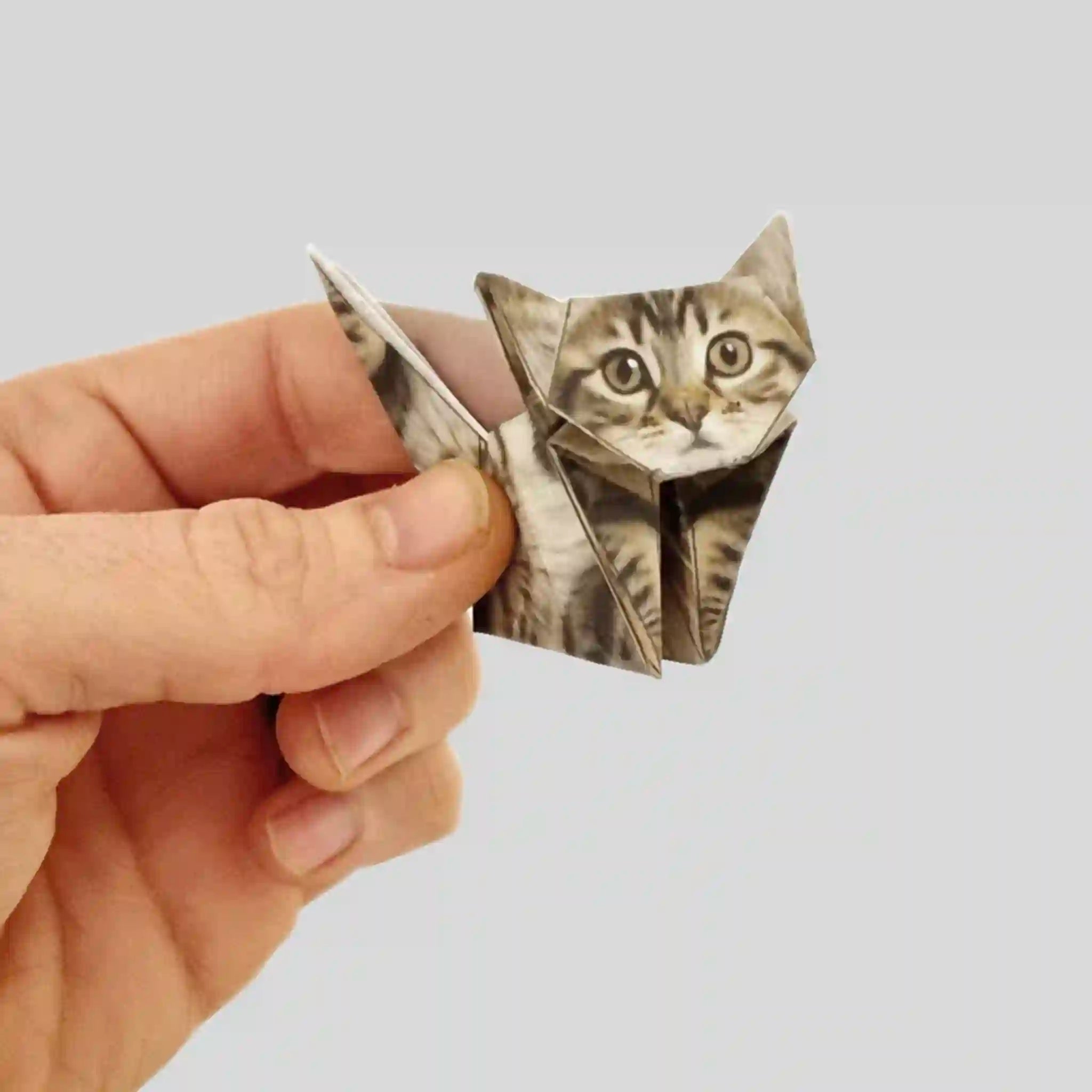 Hand holding a small origami cat against a plain background