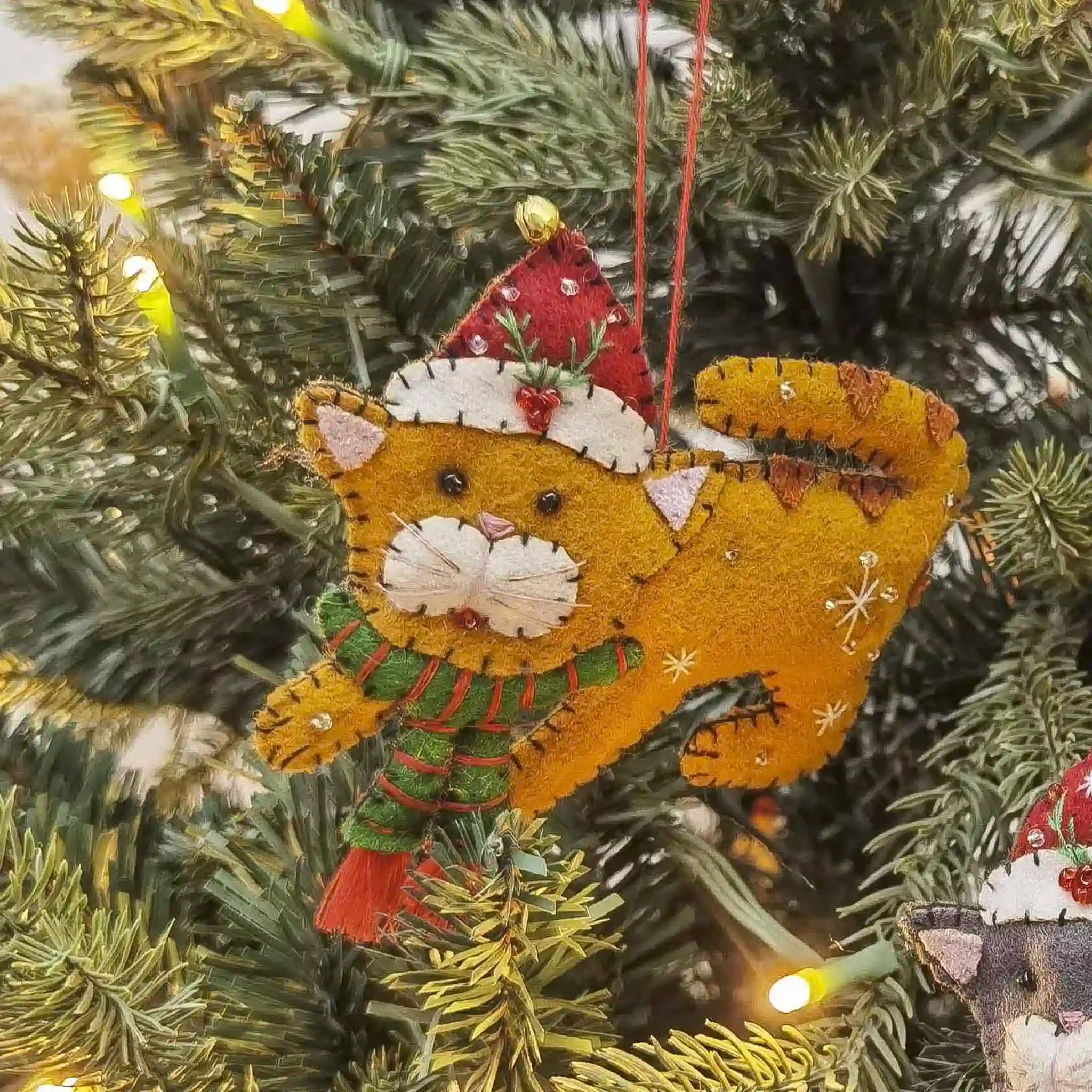 Decorative cat ornament with a Santa hat and scarf hanging on a Christmas tree.