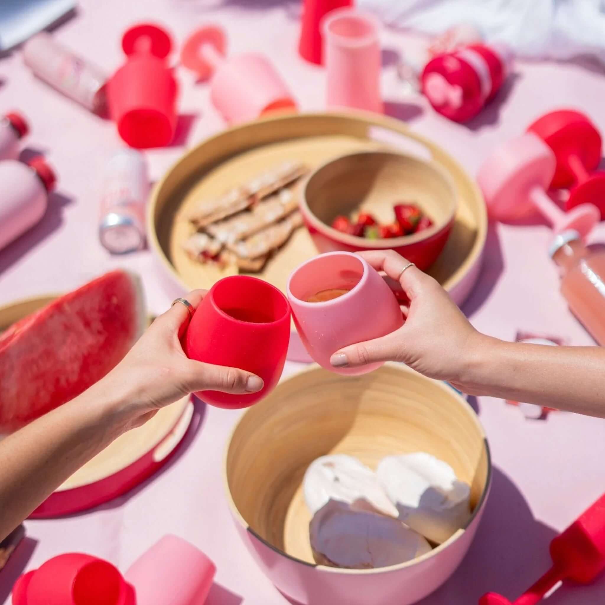 Two hands clinking Porter Green Fegg Unbreakable Glass Set - Cherry & Blush tumblers at a picnic.