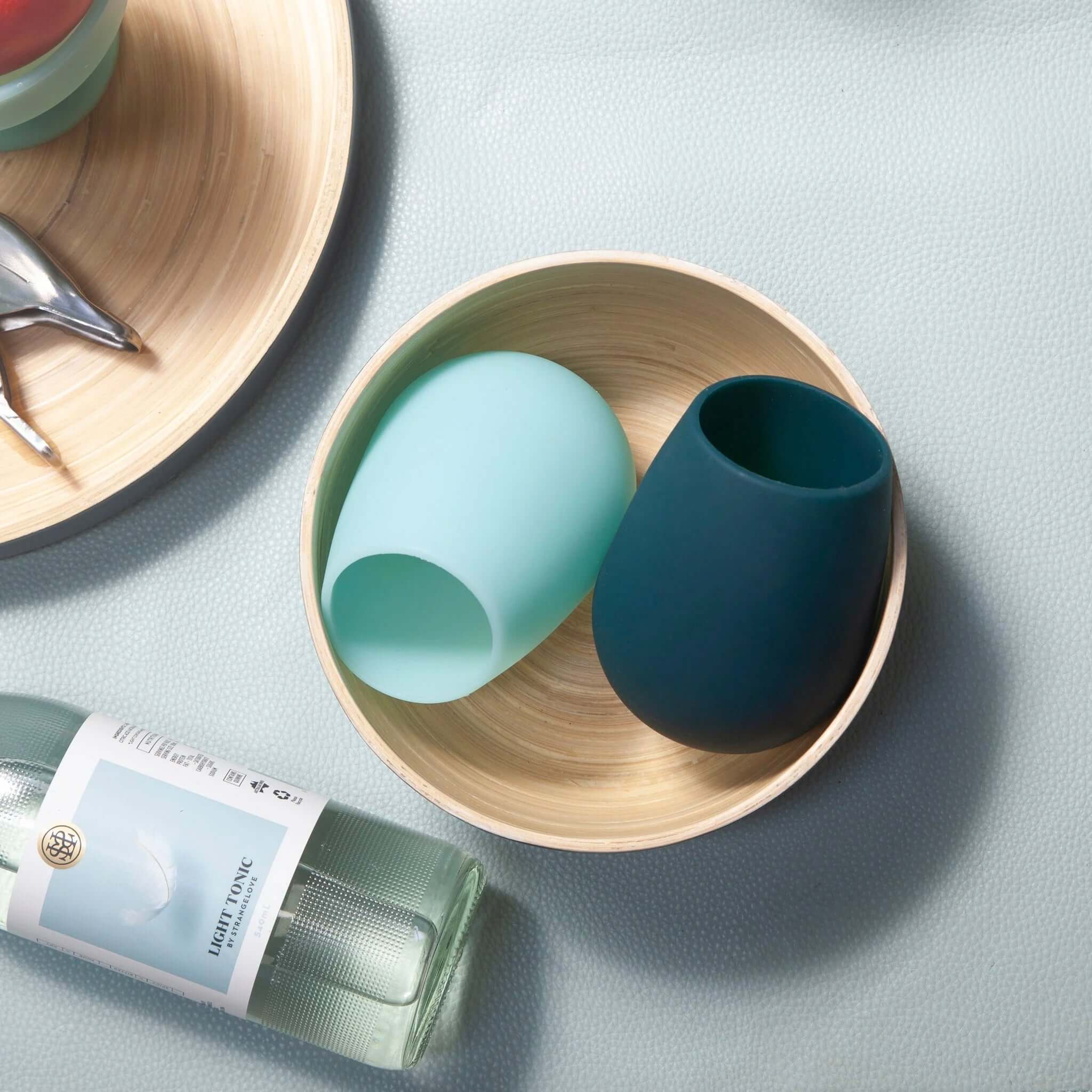 Porter Green Stemm Unbreakable Wine Glass Set - Mist & Ink in a bamboo bowl with a bottle of tonic.