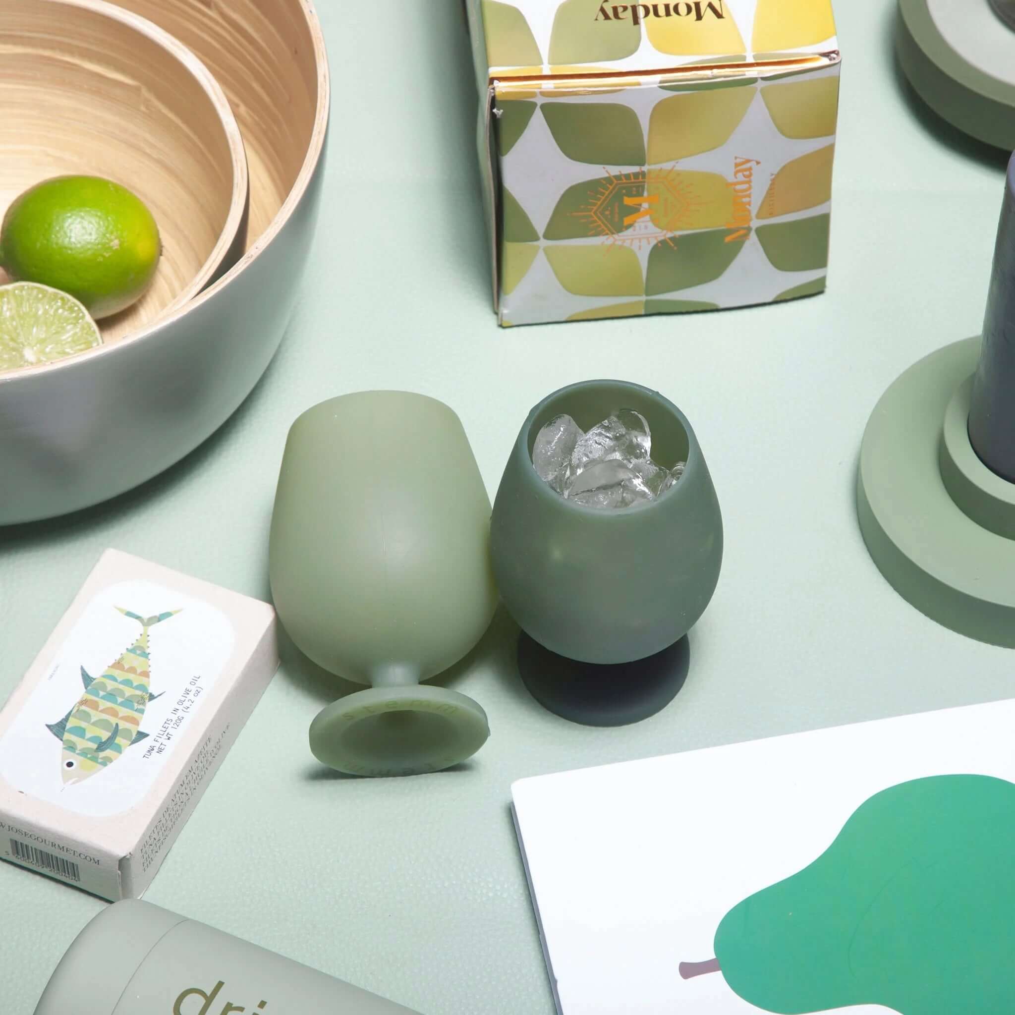 Porter Green Stemm Unbreakable Wine Glass Set - Sage & Olive stylishly displayed with accessories on a light background.