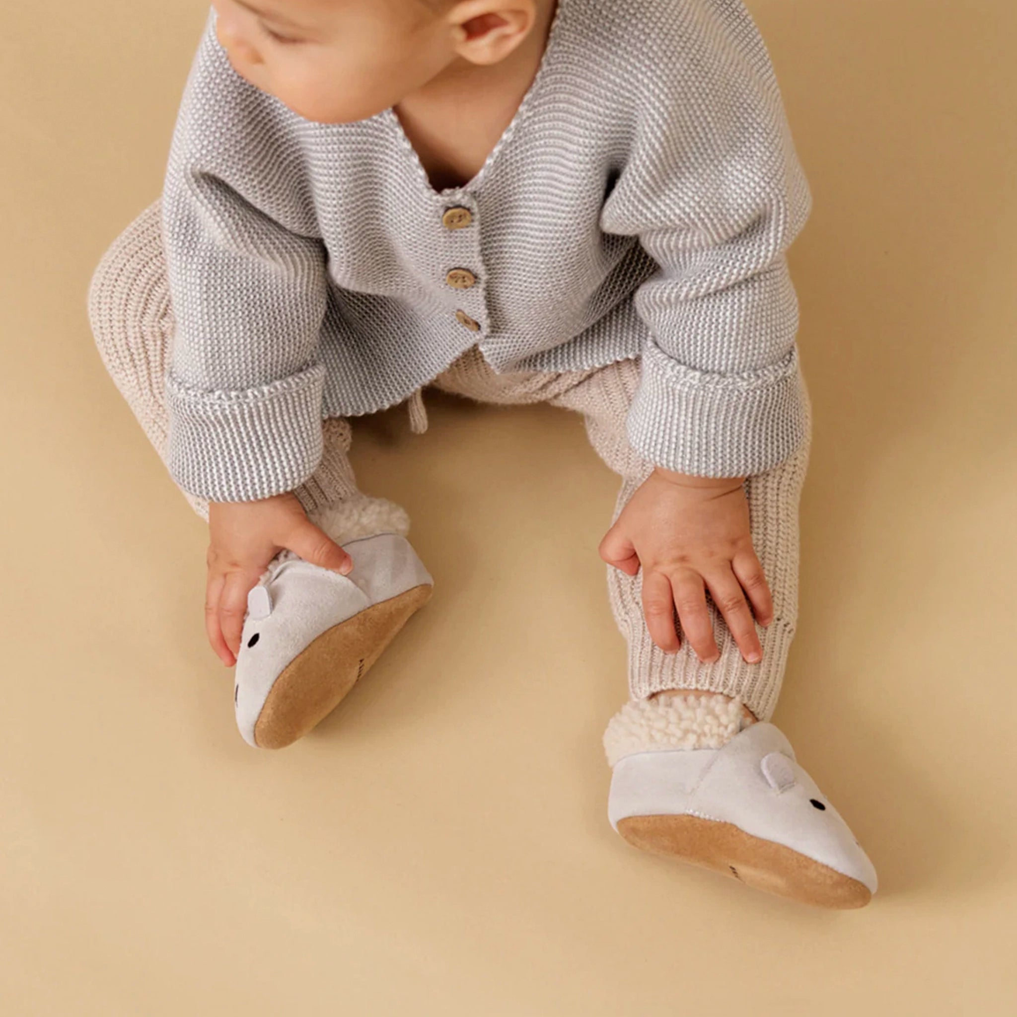 Baby wearing a knitted outfit with white shoes on a beige background