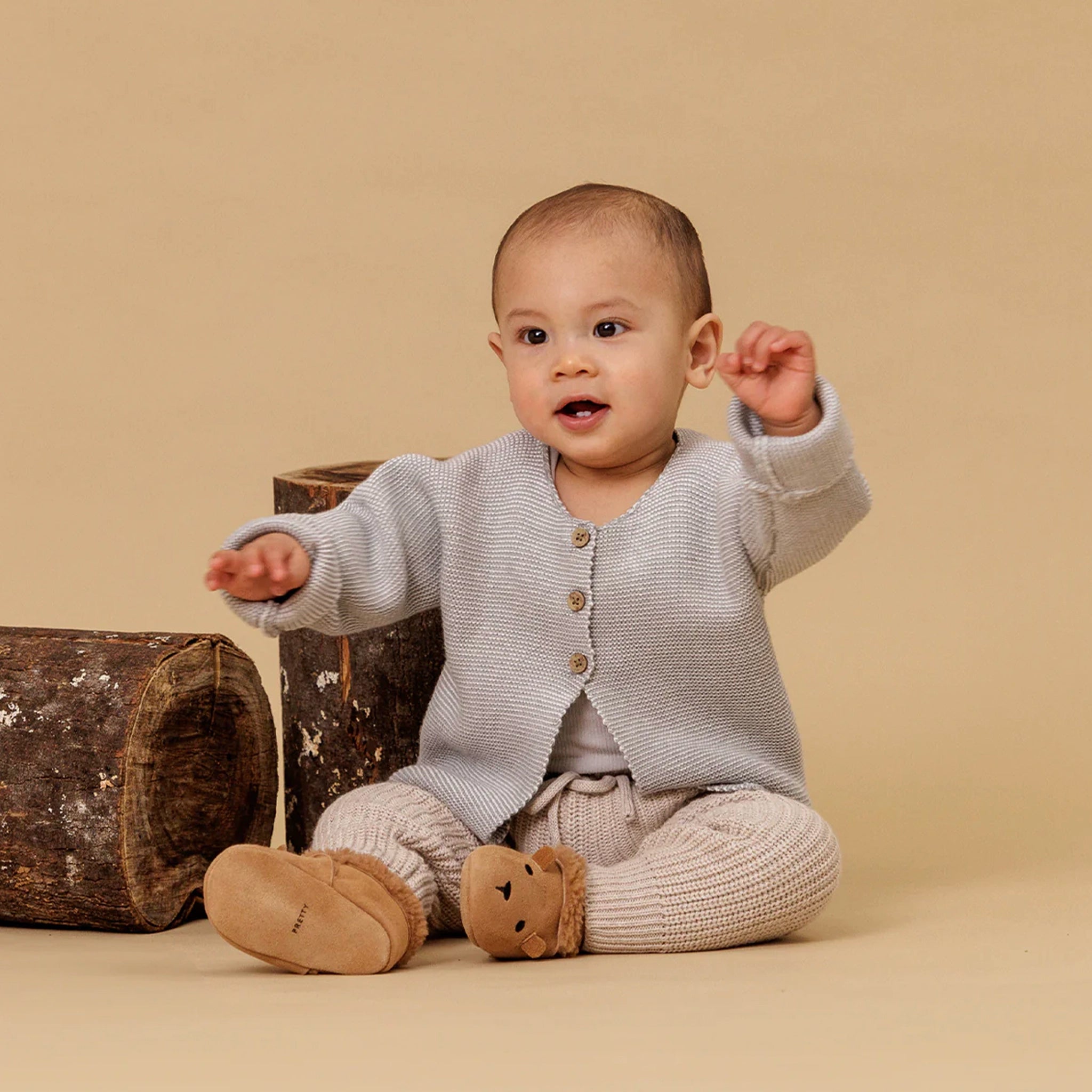 Baby wearing a light gray cardigan and beige pants sitting on a beige background