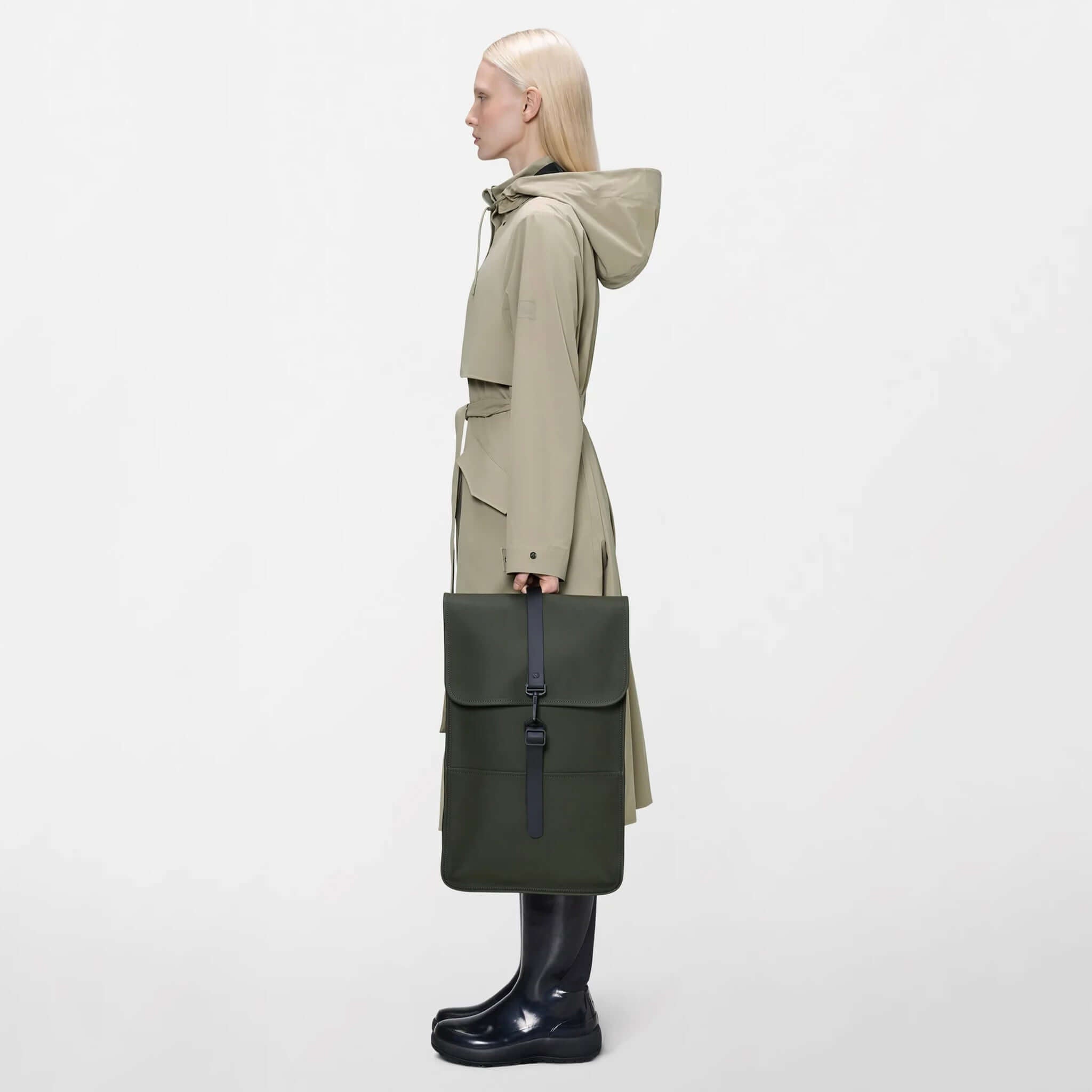 Rains Backpack - Green being held by a model in a stylish outfit, showcasing its sleek design.