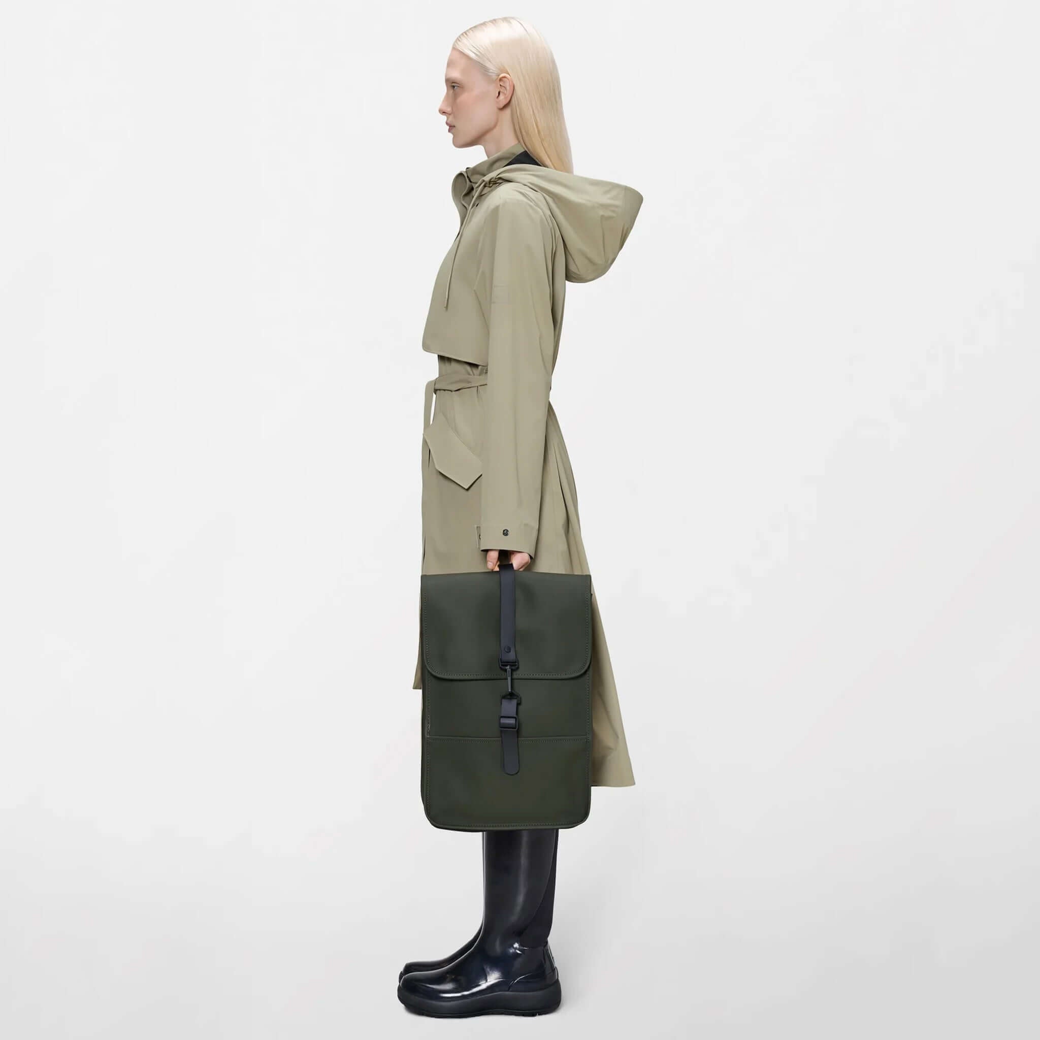 Rains Backpack Mini - Green carried by a model in a stylish trench coat, showcasing its compact and functional design.
