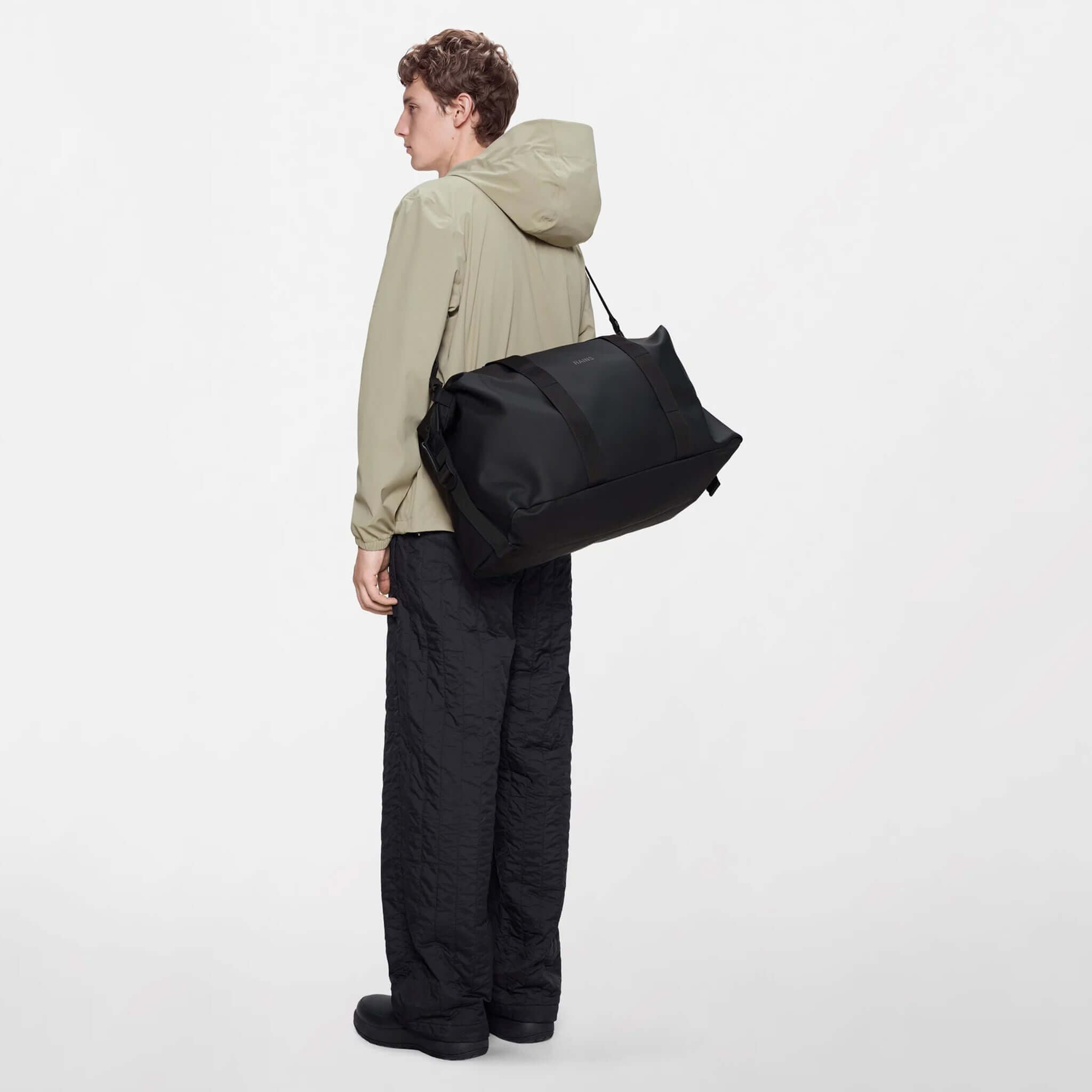 Rains Hilo Weekend Bag - Black worn by a person in casual attire, showcasing its stylish and functional design.