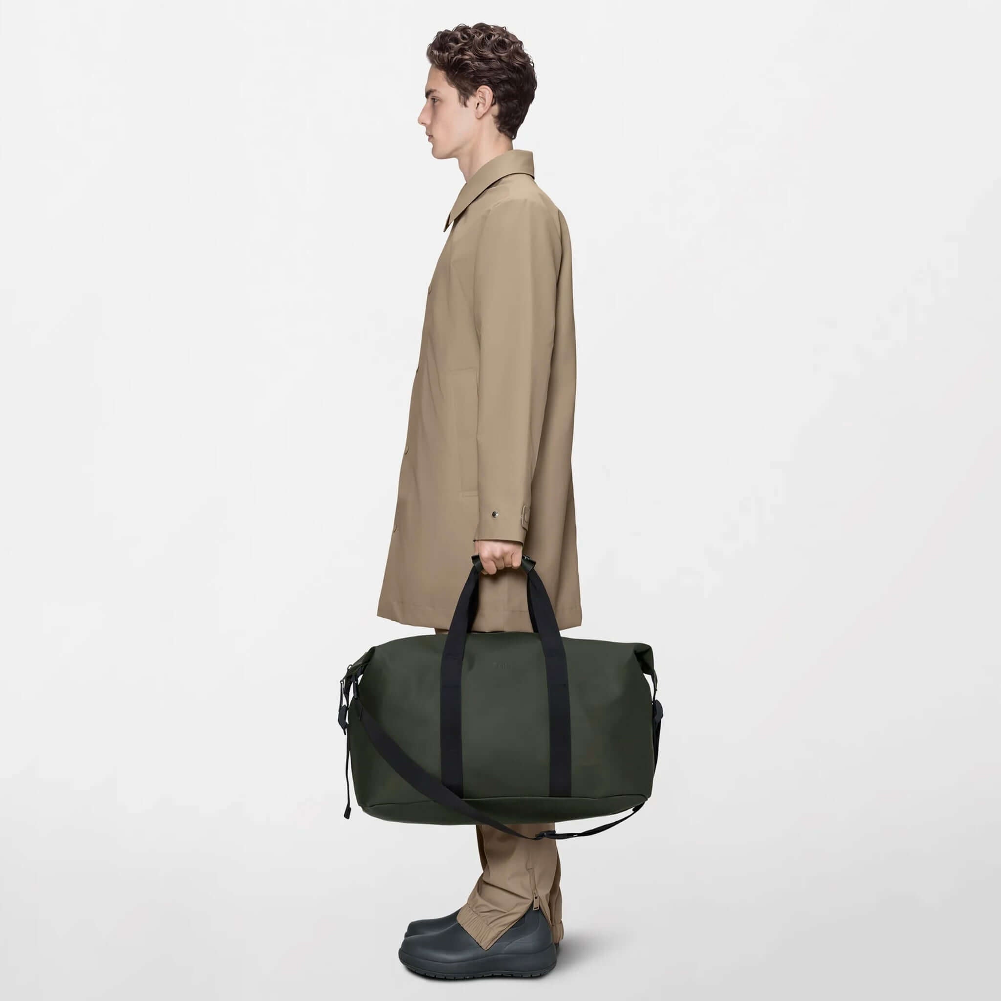 Person holding a Rains Hilo Weekend Bag - Green, showcasing its minimalist design and waterproof material.
