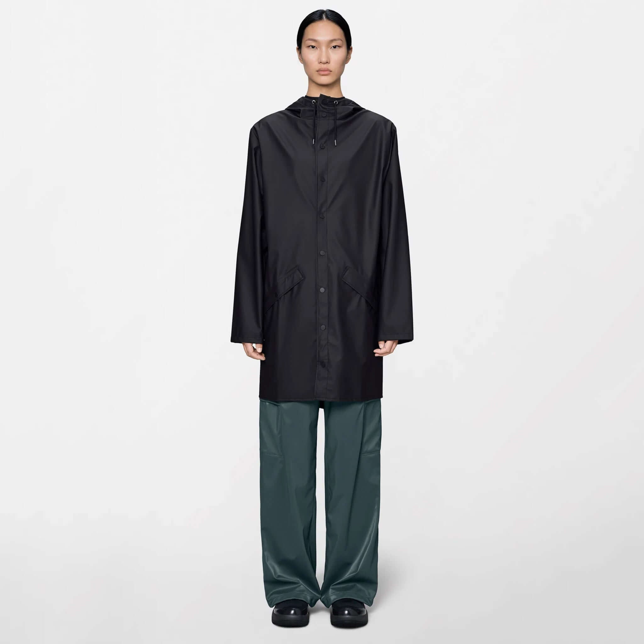 Model wearing the Rains Long Jacket - Black, showcasing its minimal design and extended length for extra coverage.
