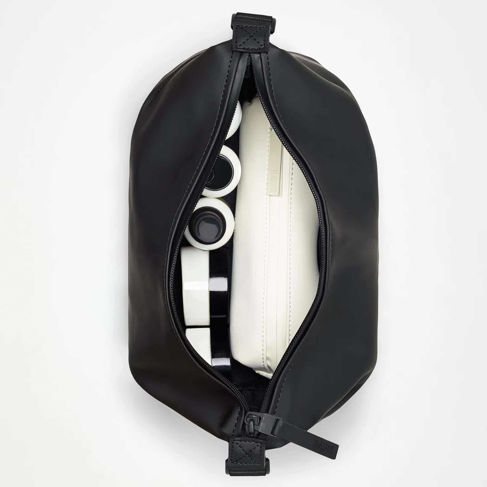 Rains Wash Bag Small - Black opened, showcasing toiletry items and cosmetics inside.