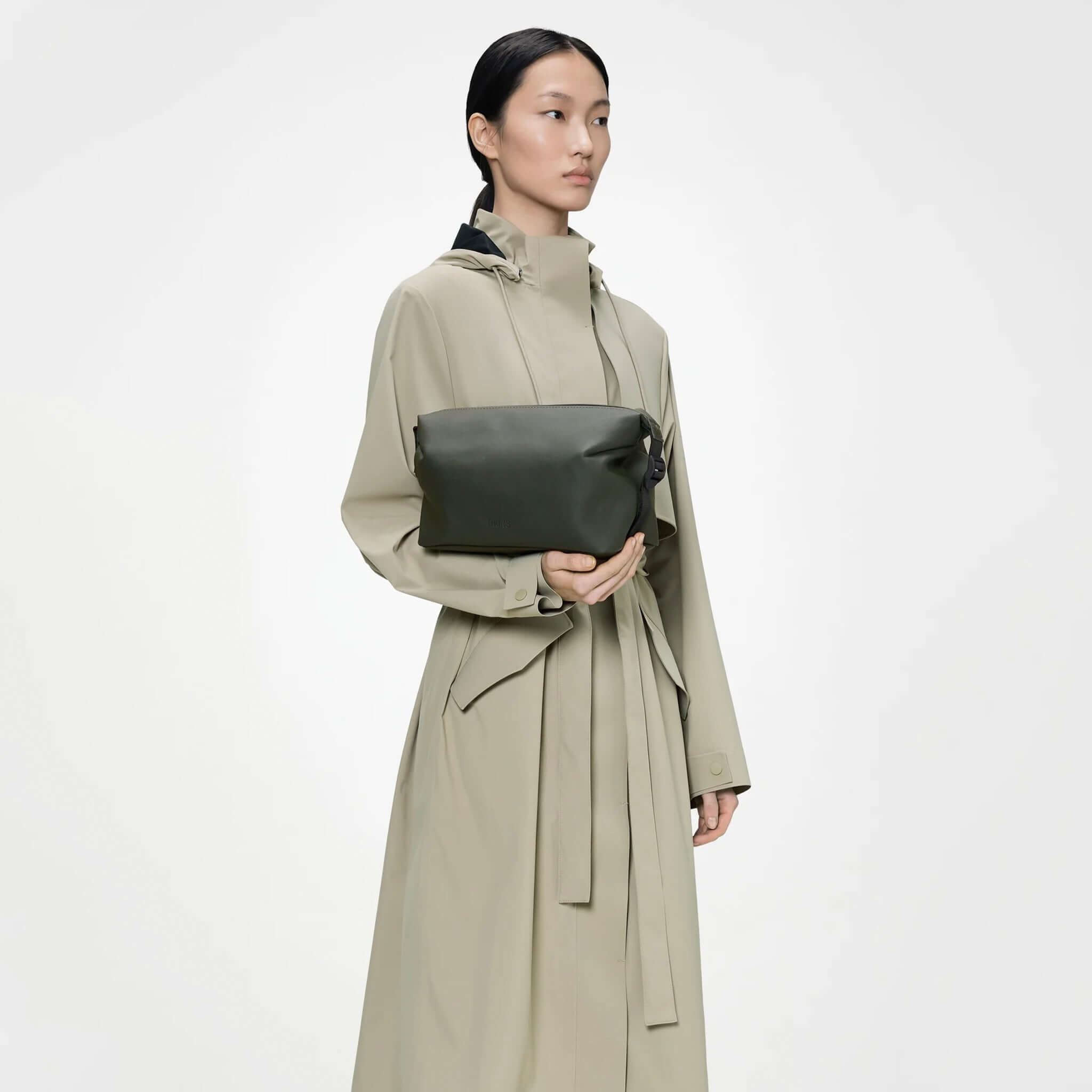 Rains Wash Bag Small - Green held by a model in a stylish coat against a neutral background.