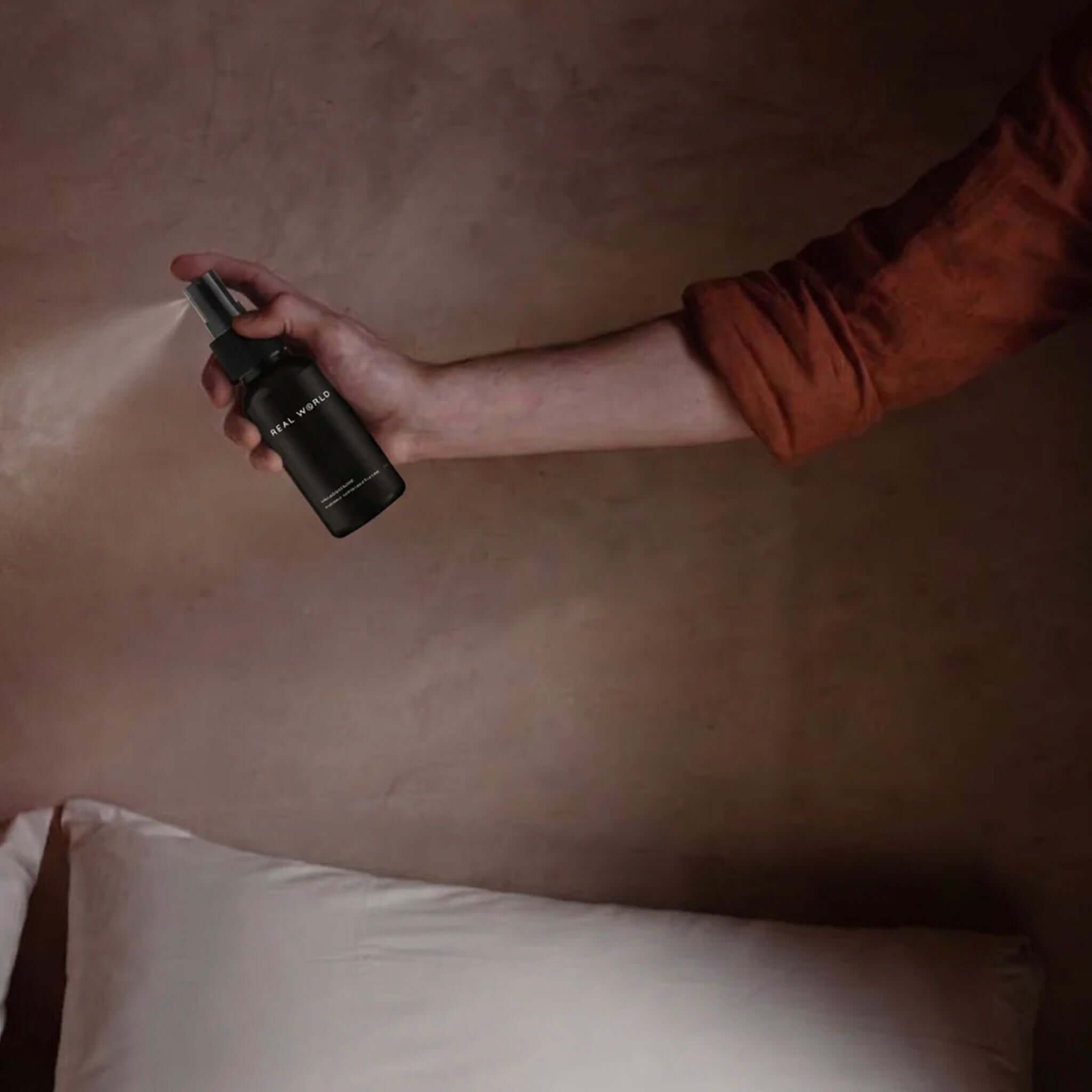 Hand spraying Real World Pillow Mist - Kawakawa, Chamomile & Pepper over a pillow for better sleep.