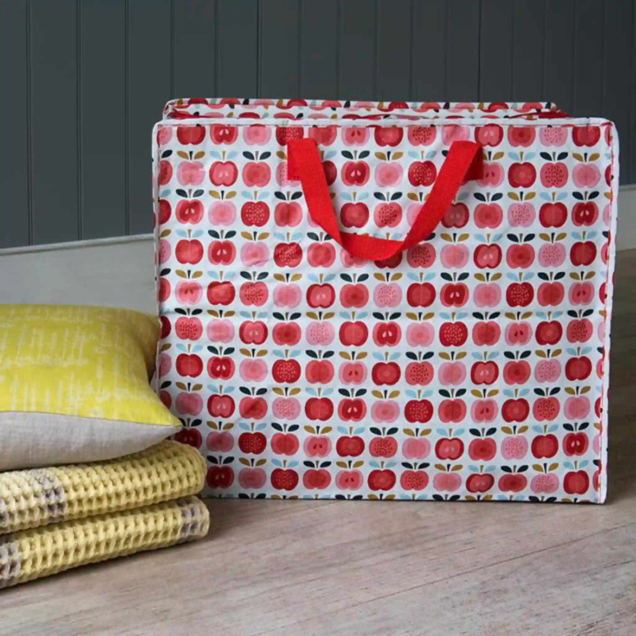 Tote bag with red apple pattern on a wooden surface with yellow fabric and gray wall background