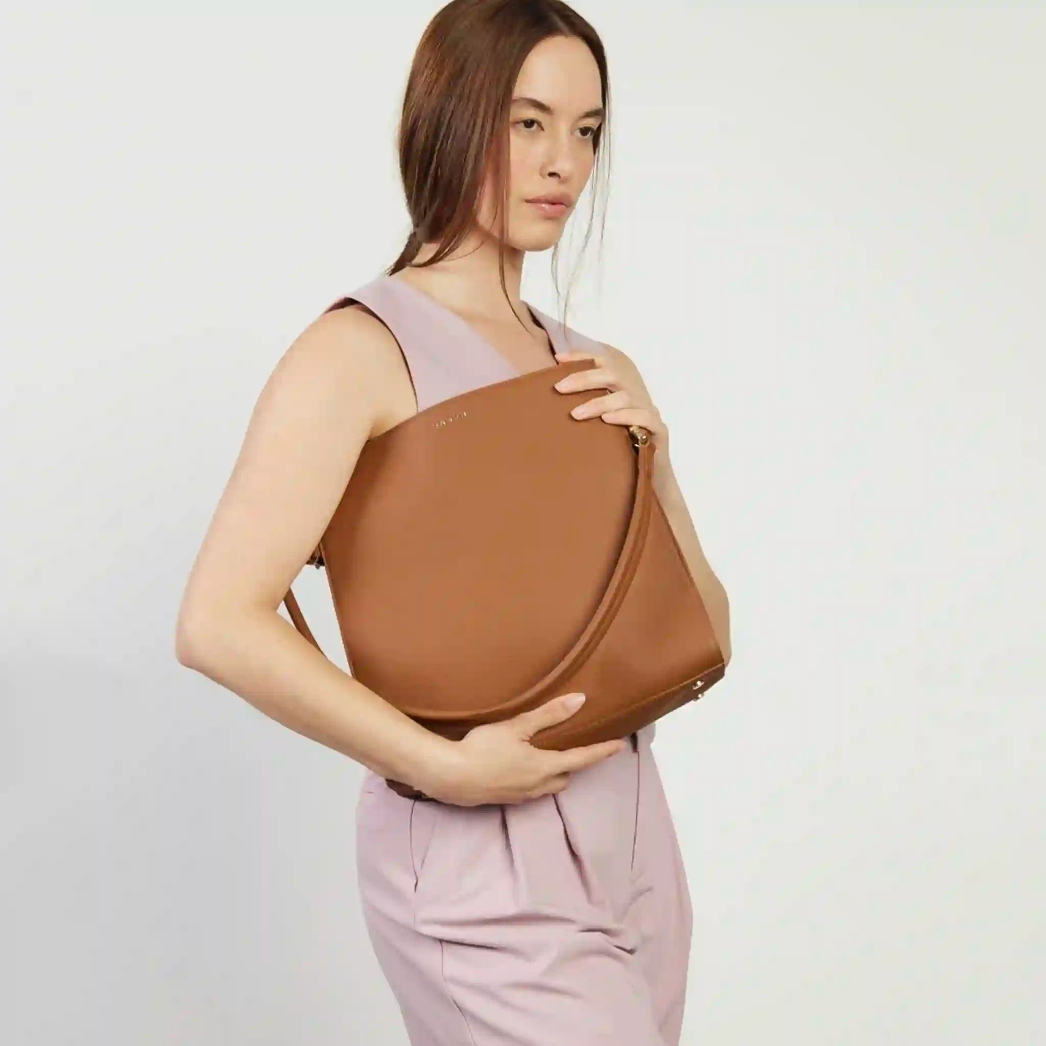 Woman holding a brown leather bag against a plain background