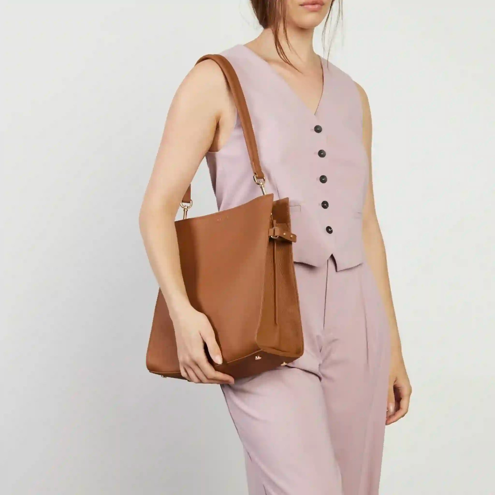Woman holding a brown leather bag against a plain background