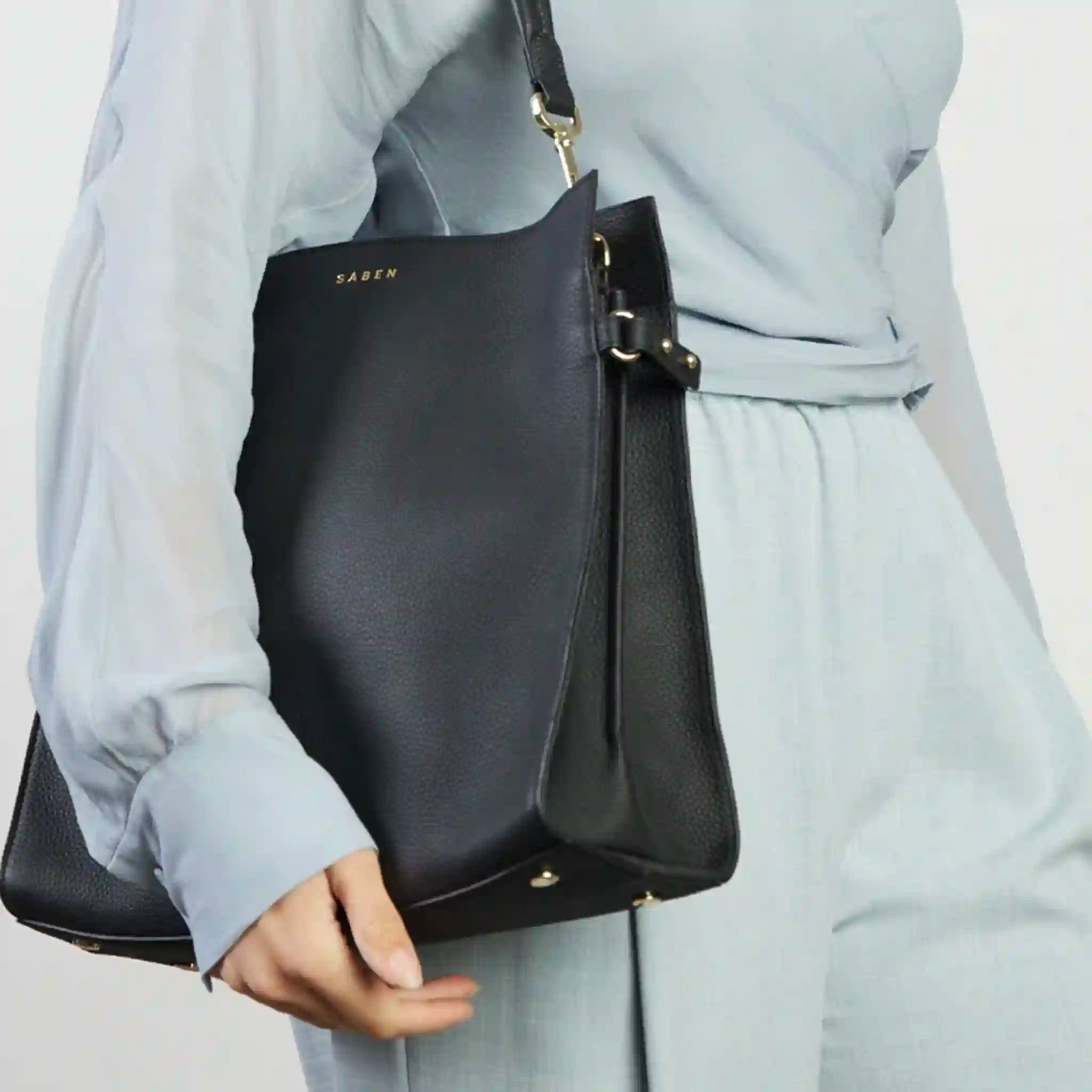 Person holding a black handbag with 'Saben' branding against a neutral background