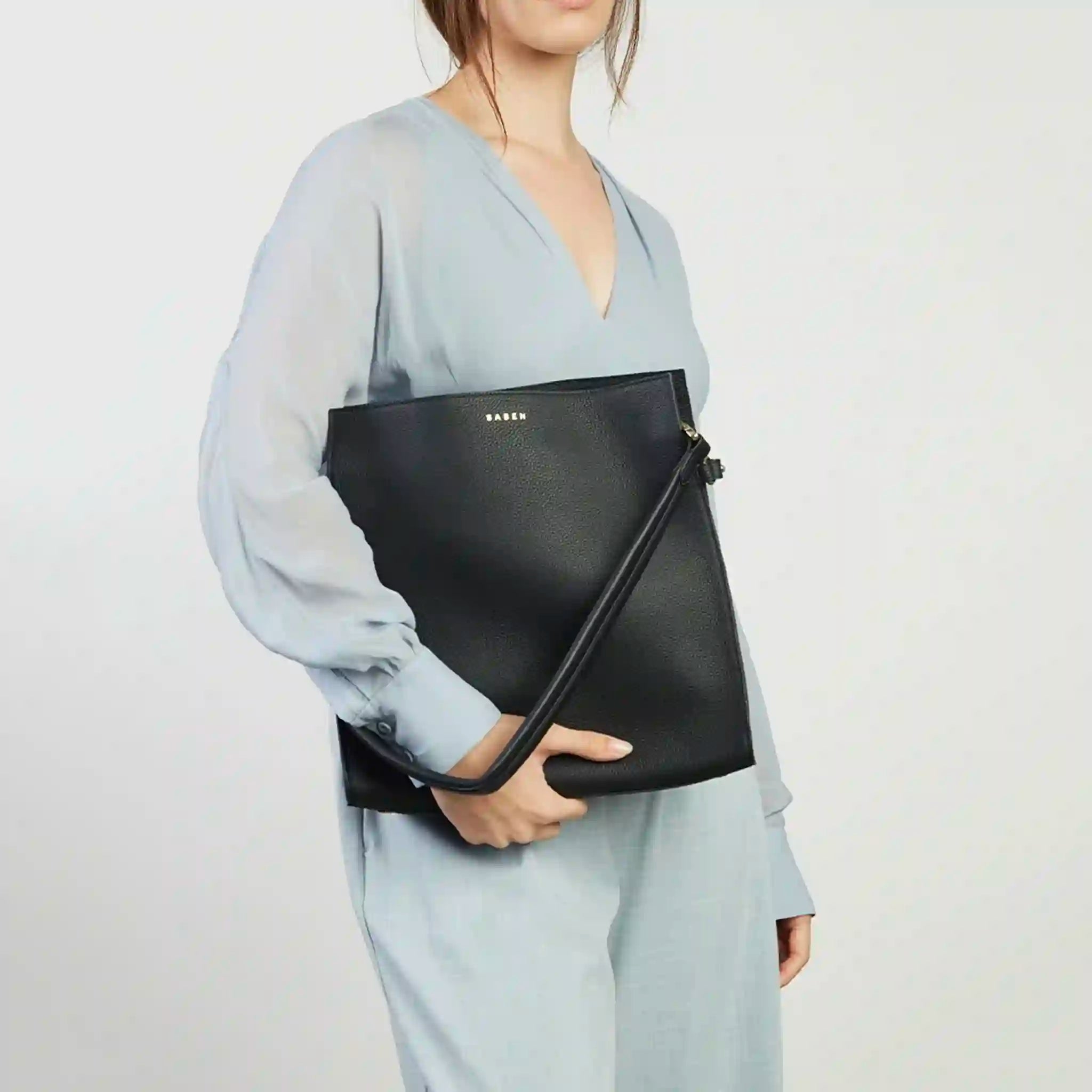 Person holding a black clutch bag against a plain background