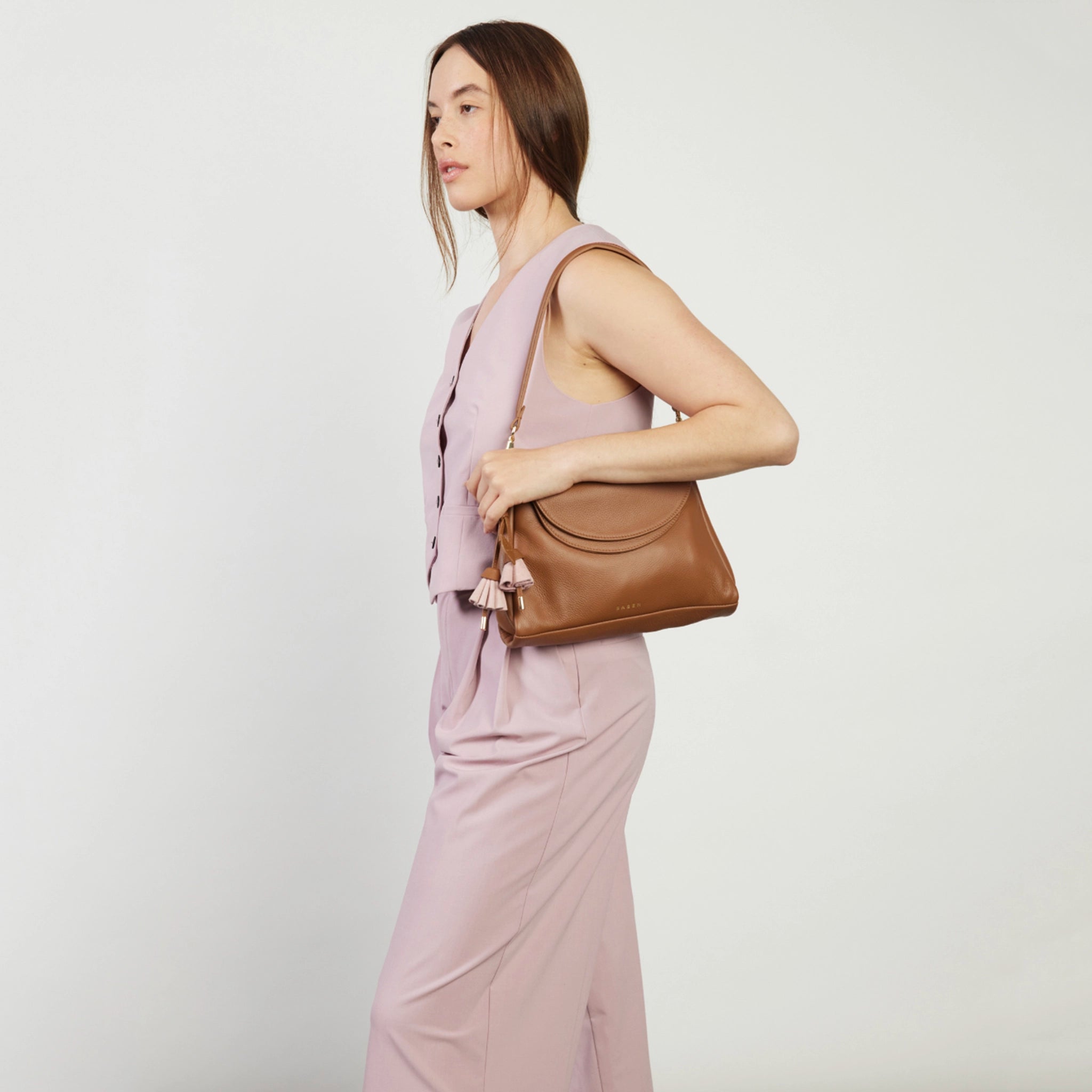 Woman holding a brown handbag against a plain background