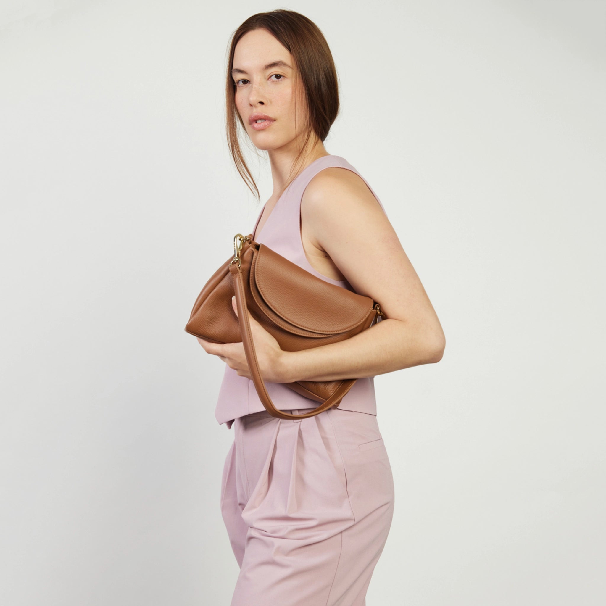 Woman holding a brown leather handbag against a plain background