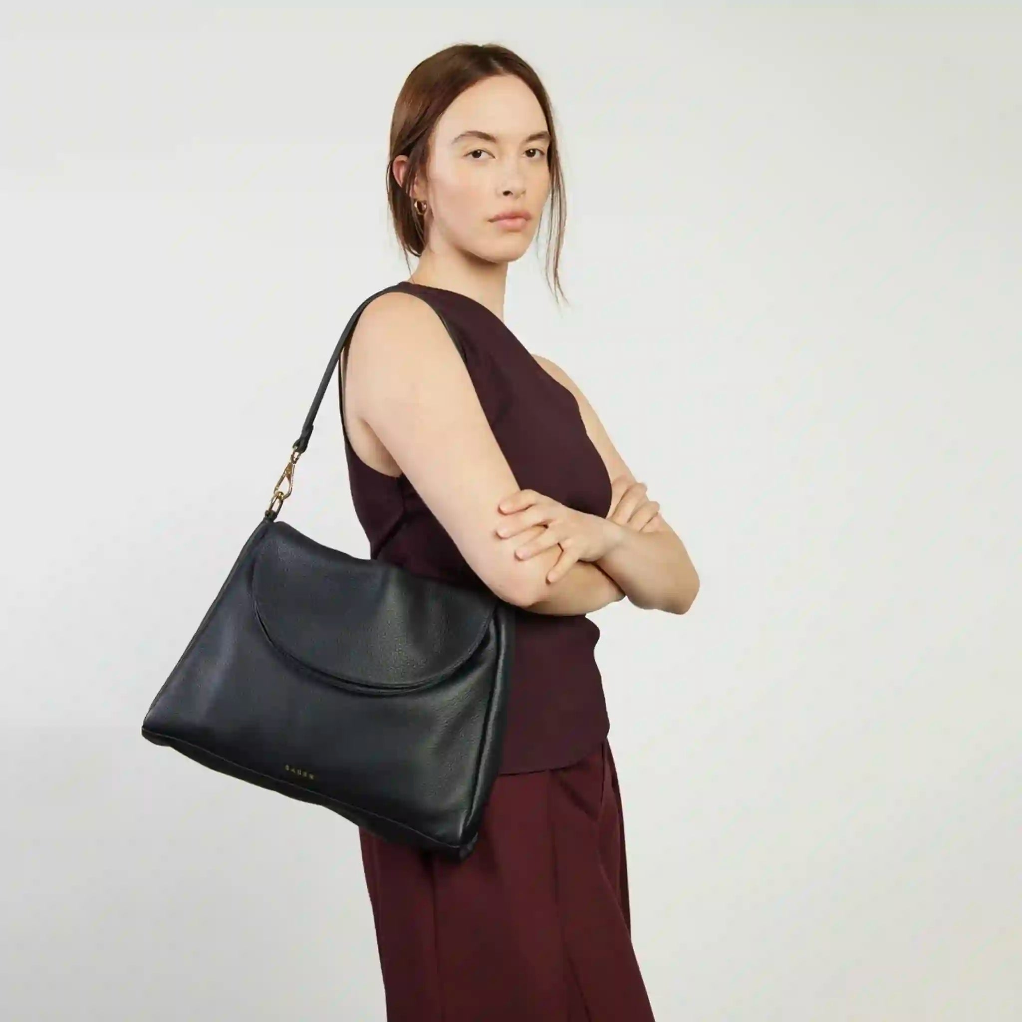 Woman holding a black handbag against a plain background