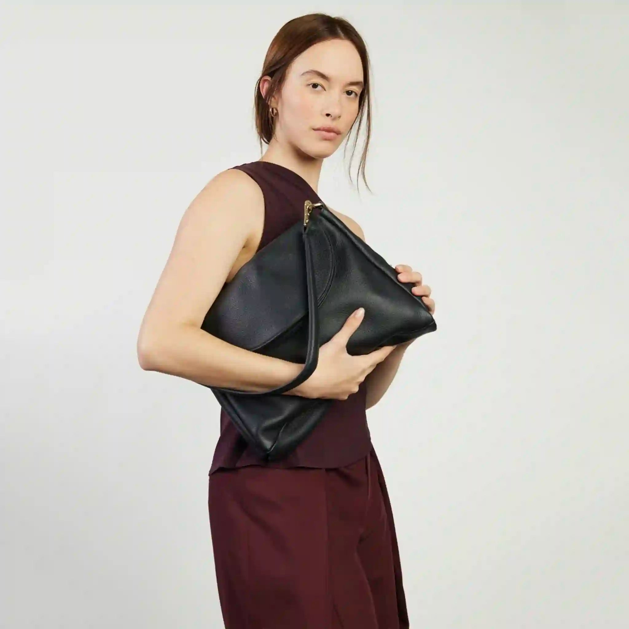Woman holding a black clutch against a plain background