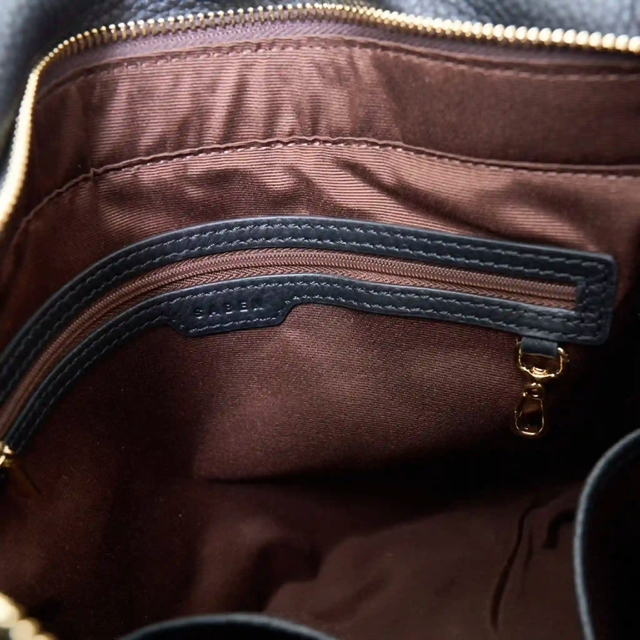 Close-up of a brown leather bag with a gold zipper and visible brand name.