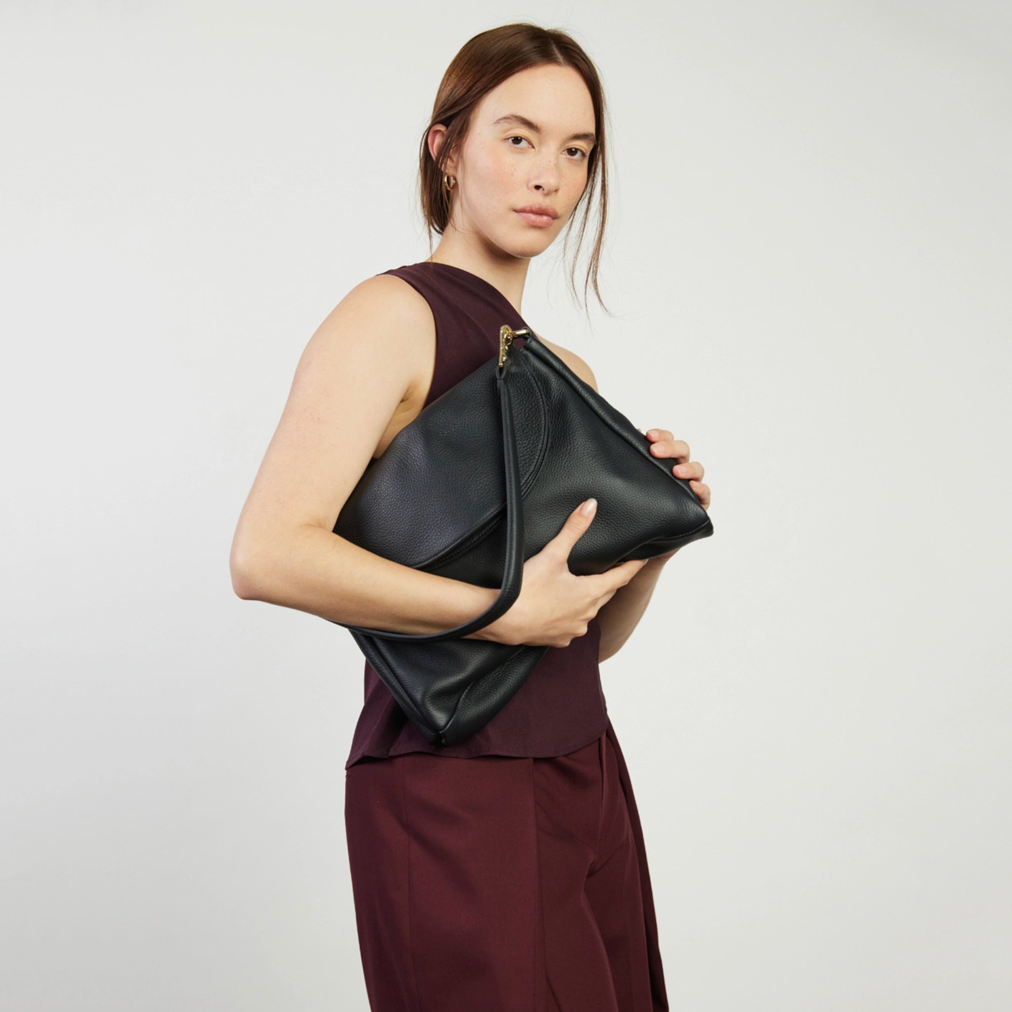 Woman holding a black leather clutch against a plain background