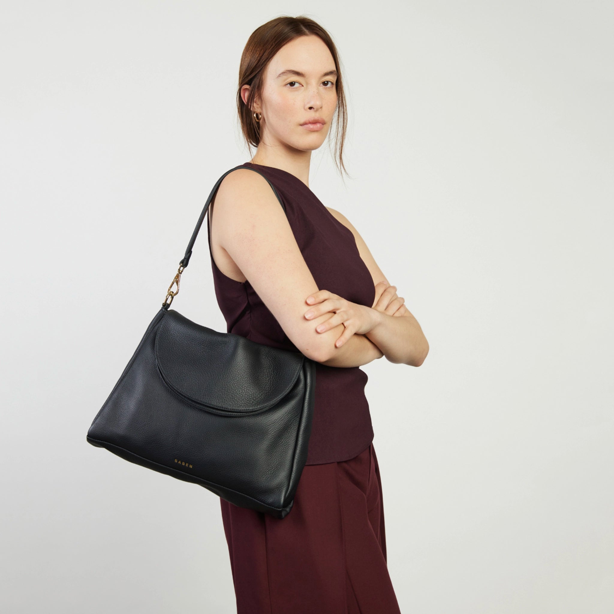 Woman holding a black handbag against a plain background