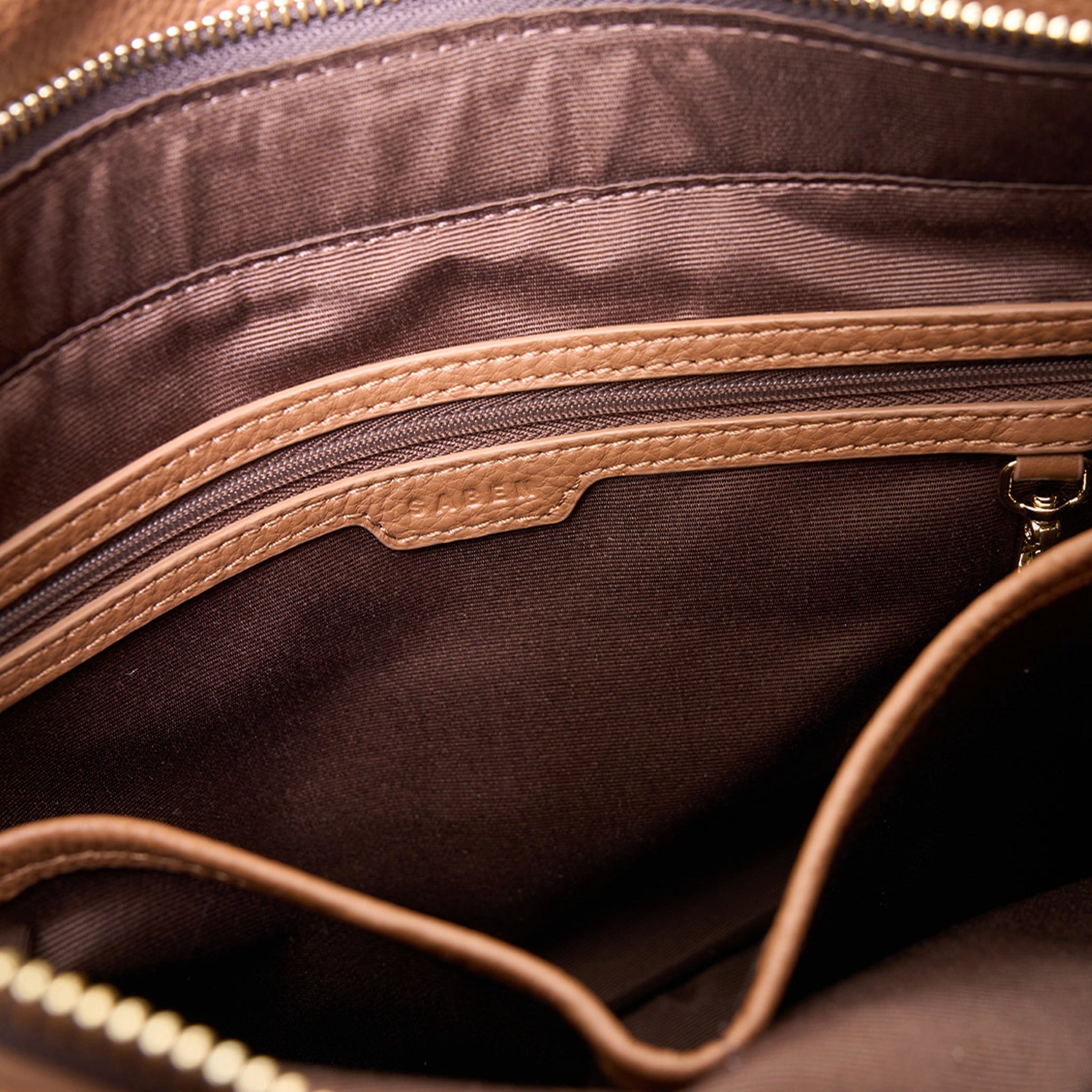 Close-up of a brown leather bag with visible stitching and zipper.