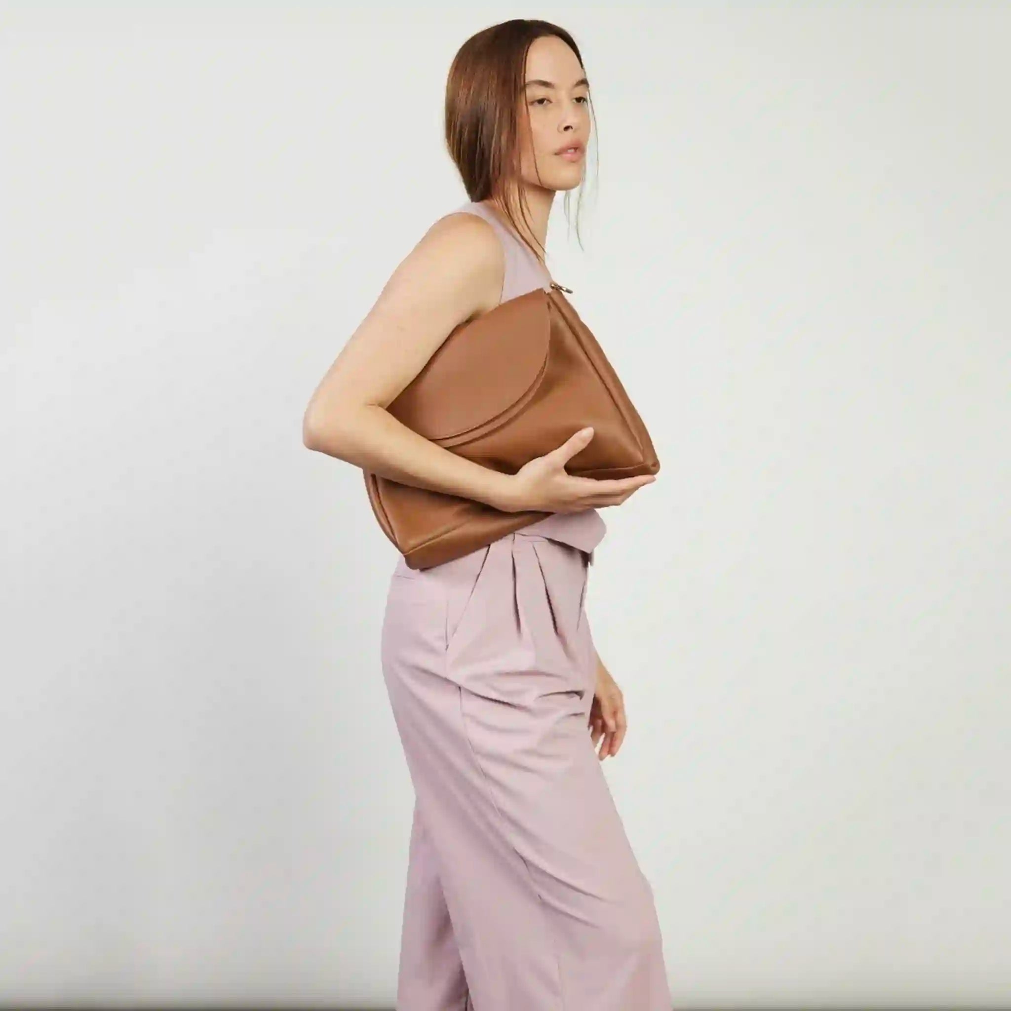 Woman holding a brown leather clutch bag against a plain background