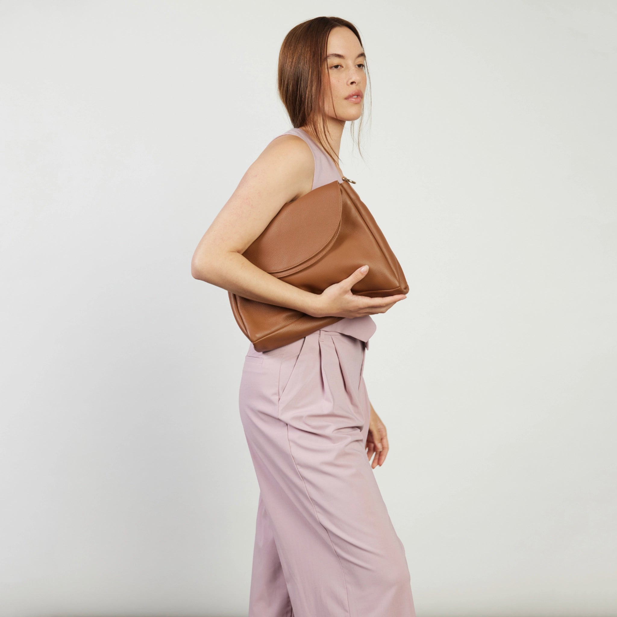 Woman holding a brown leather bag against a plain background