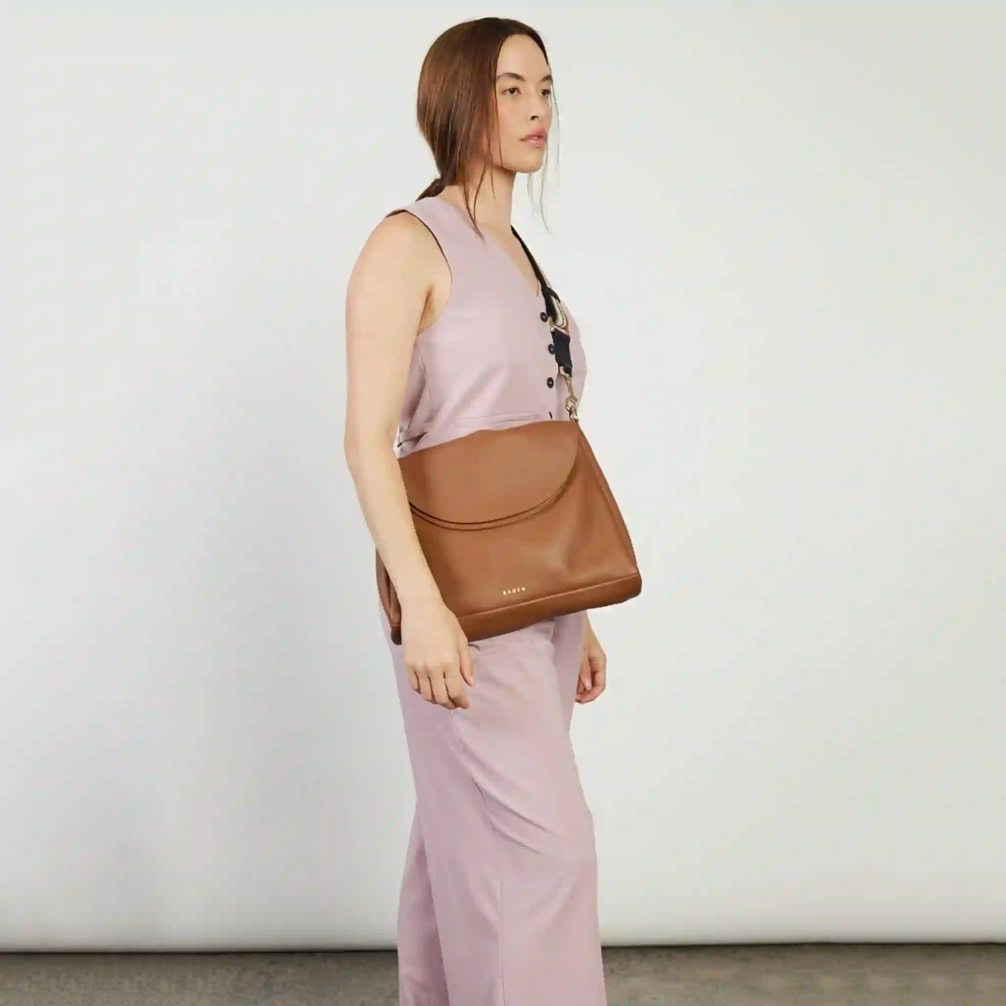 Woman holding a brown leather bag against a plain background
