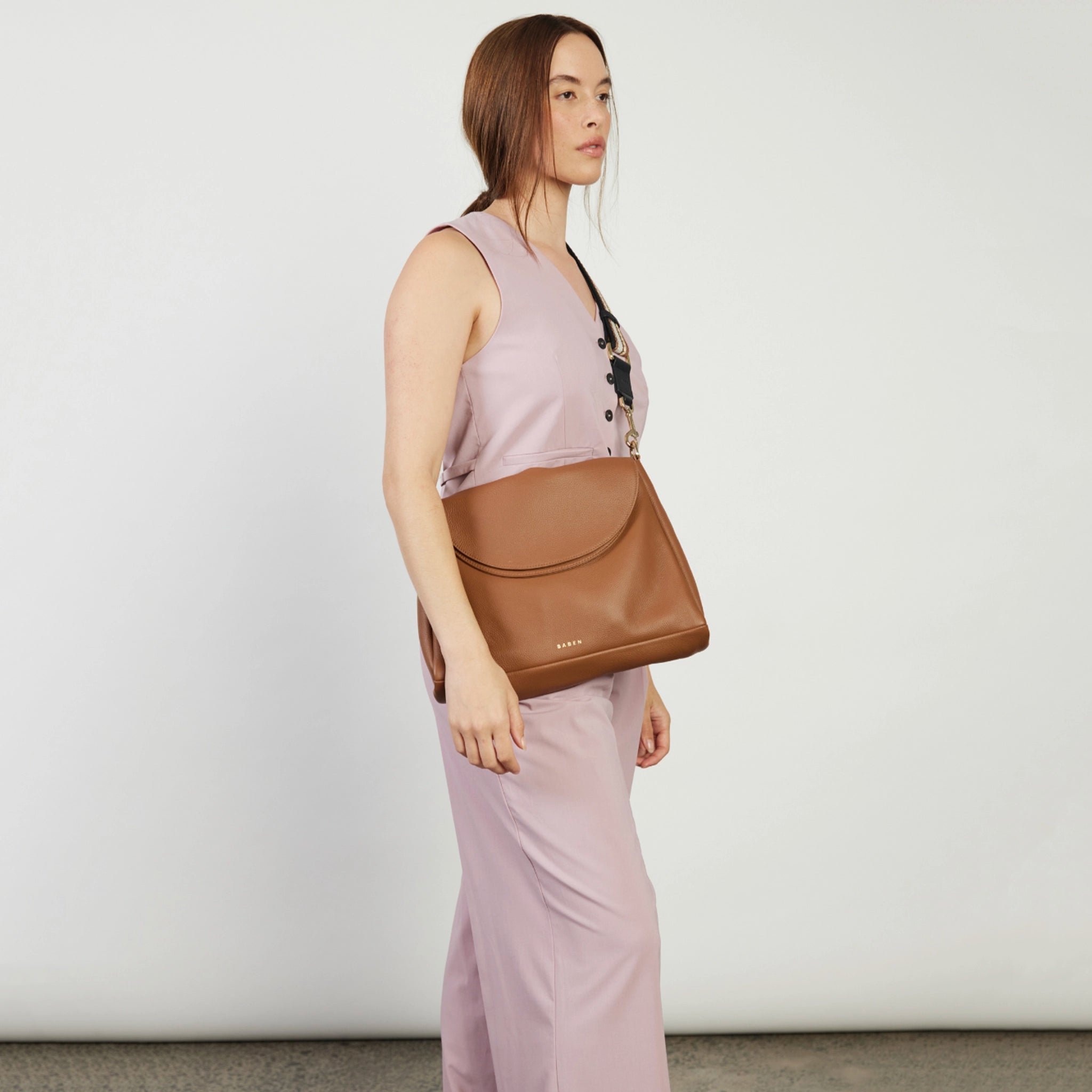Woman holding a brown leather bag against a plain background