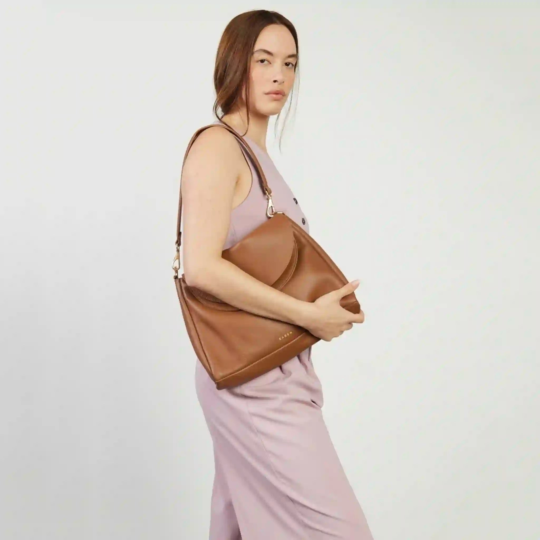 Woman holding a brown leather handbag against a plain background