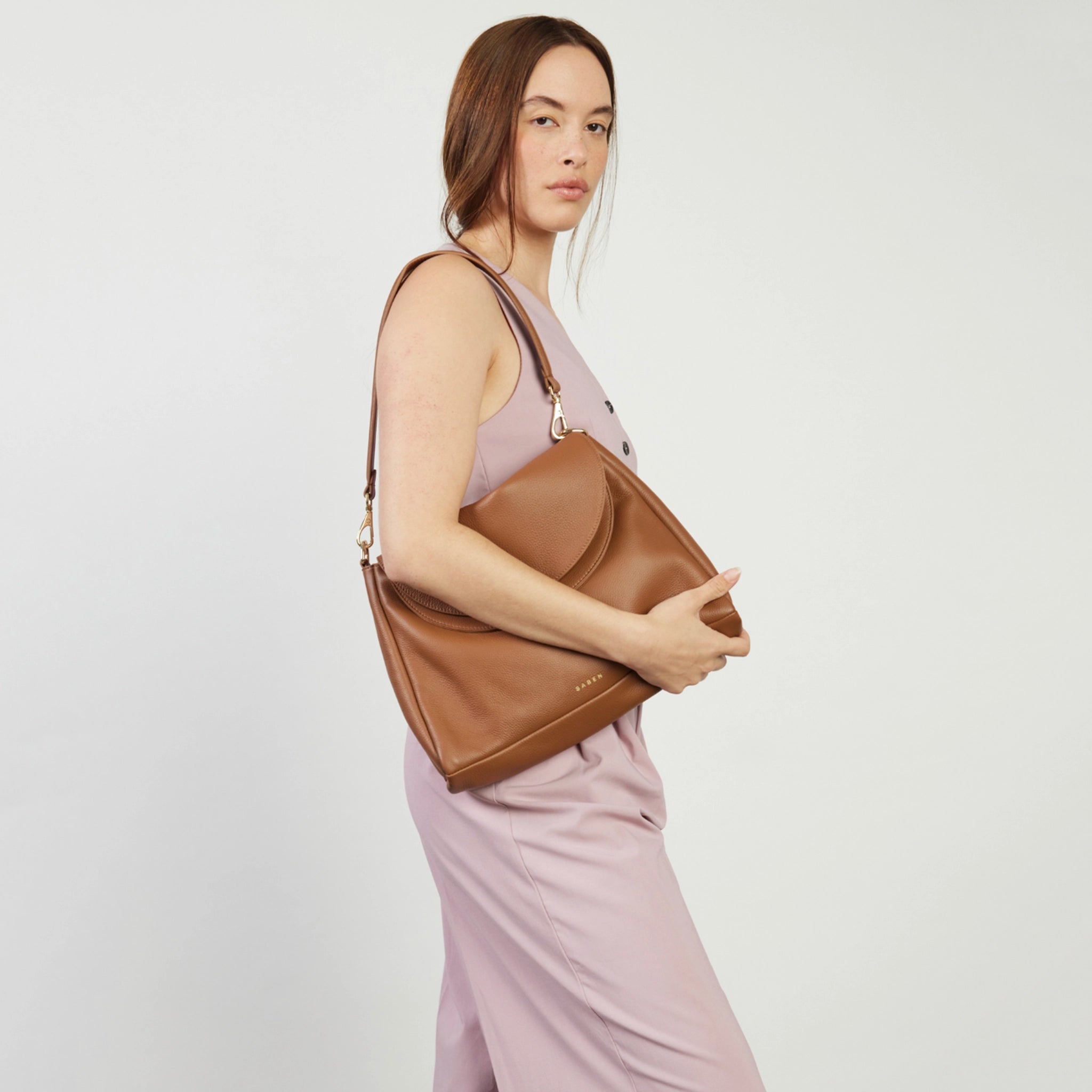 Woman holding a brown leather handbag against a plain background