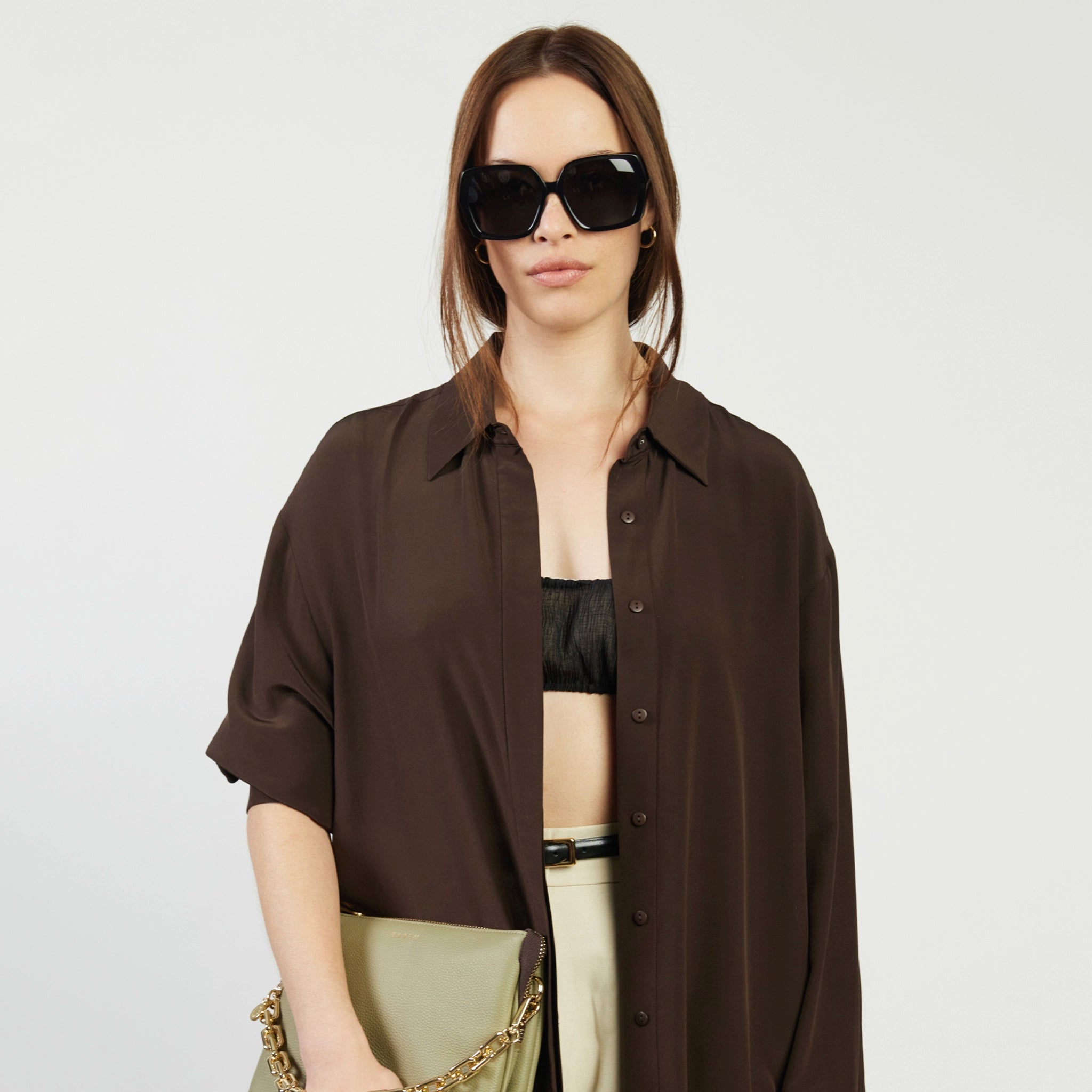 Woman wearing a brown shirt over a black top and beige pants on a white background