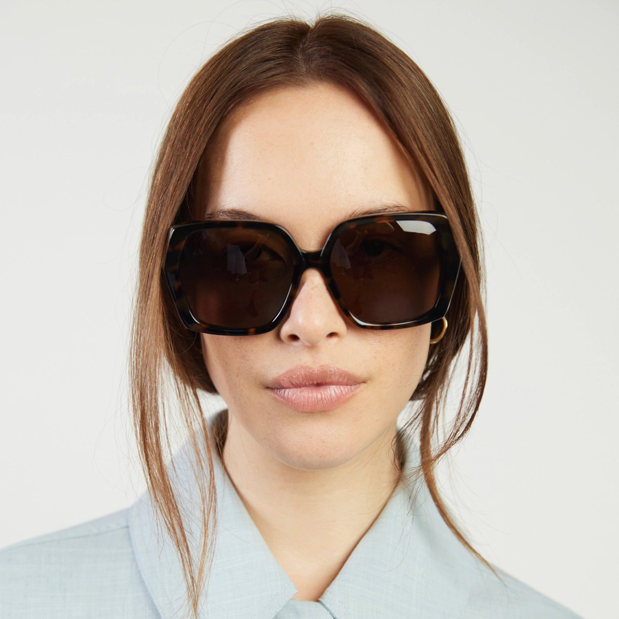 Woman wearing dark sunglasses against a plain background