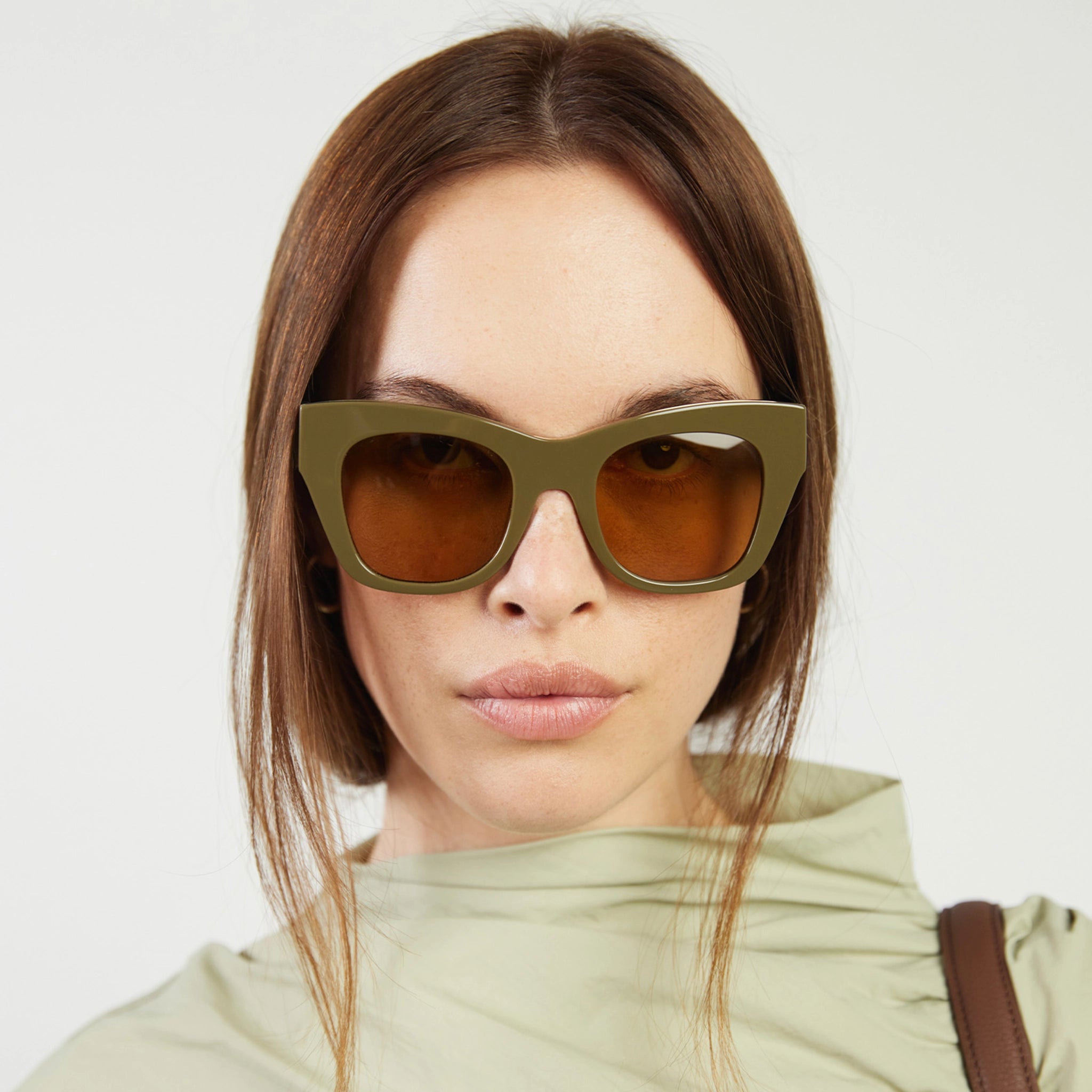 Woman wearing green sunglasses with a plain background