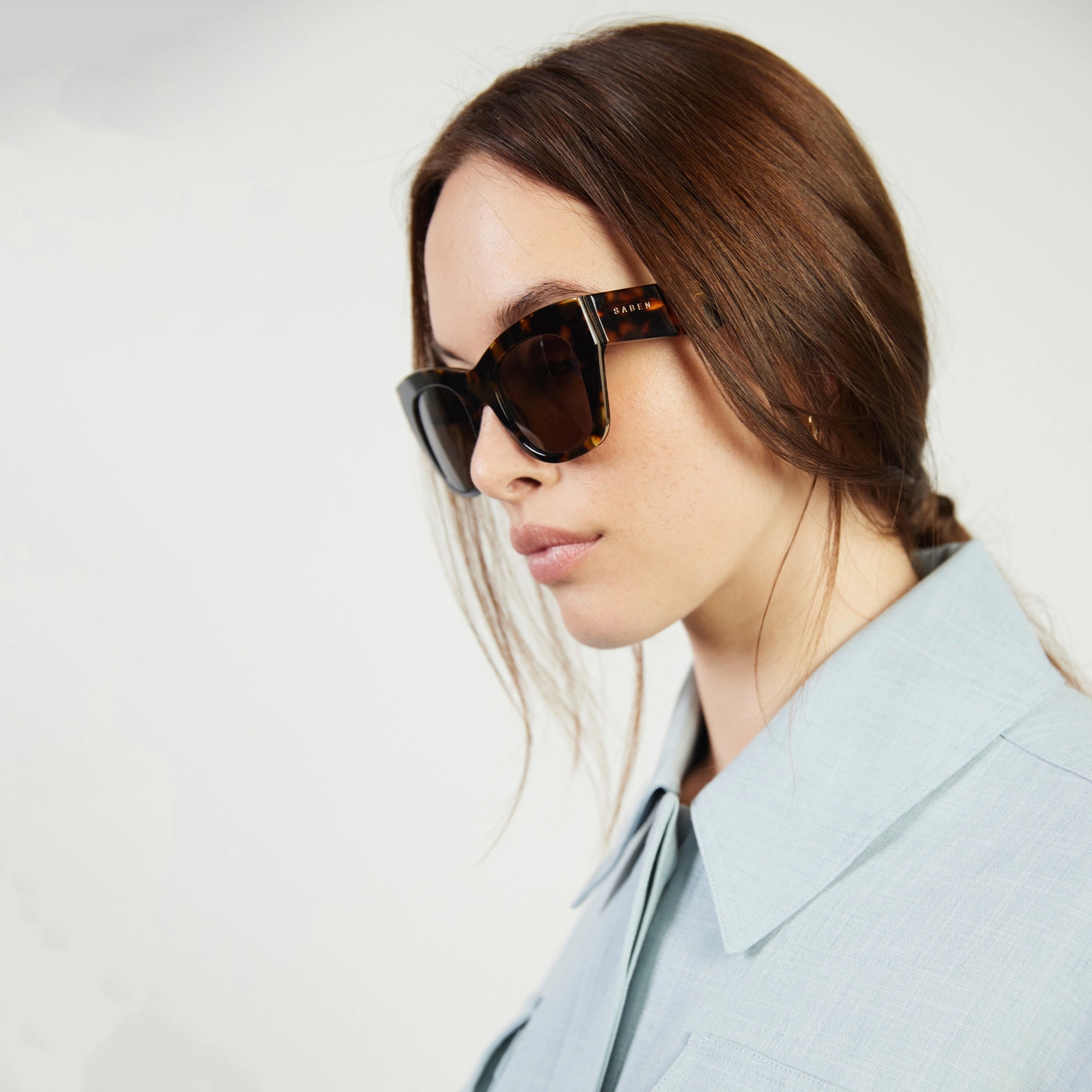Woman wearing sunglasses and a light gray coat on a white background