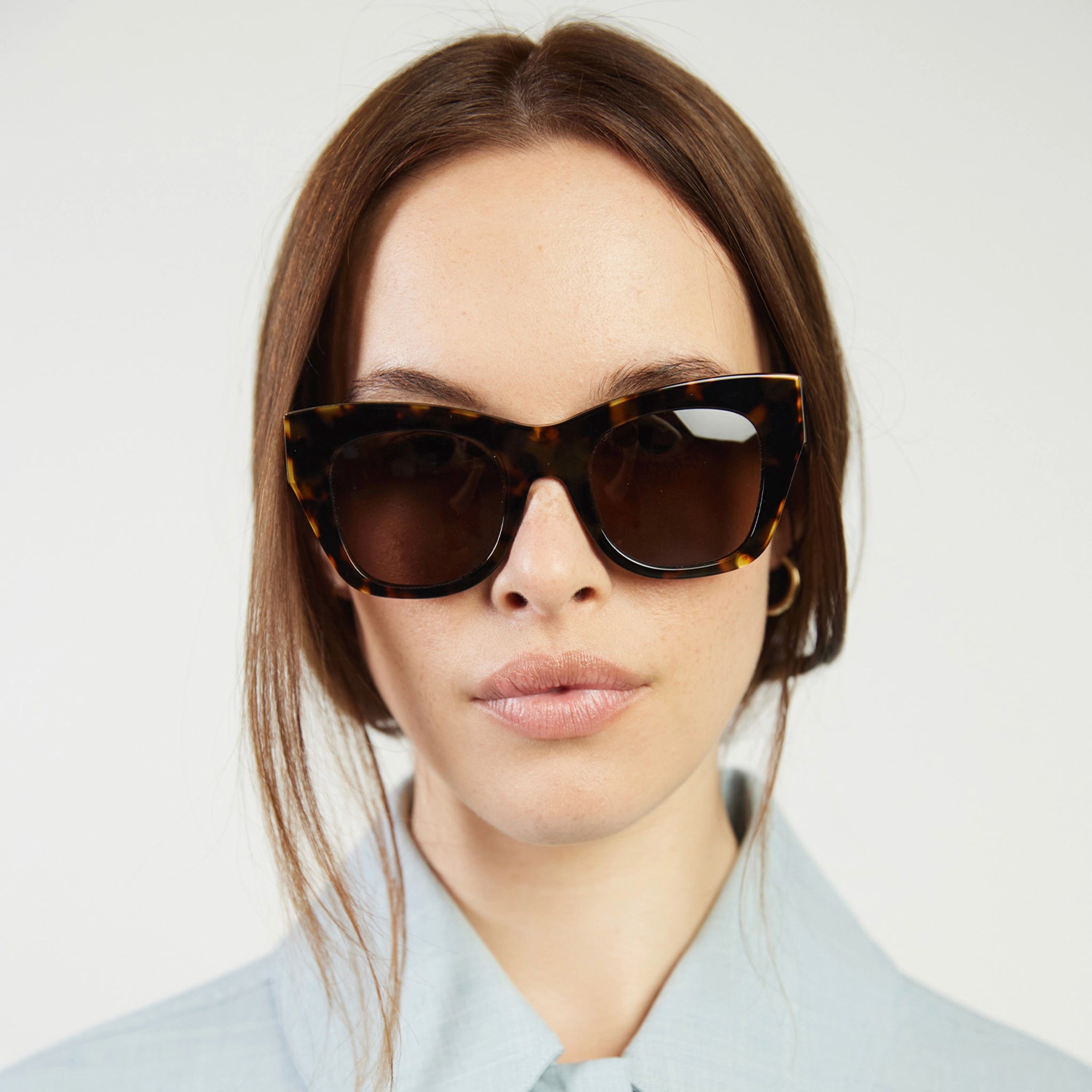 Woman wearing tortoiseshell sunglasses against a plain background