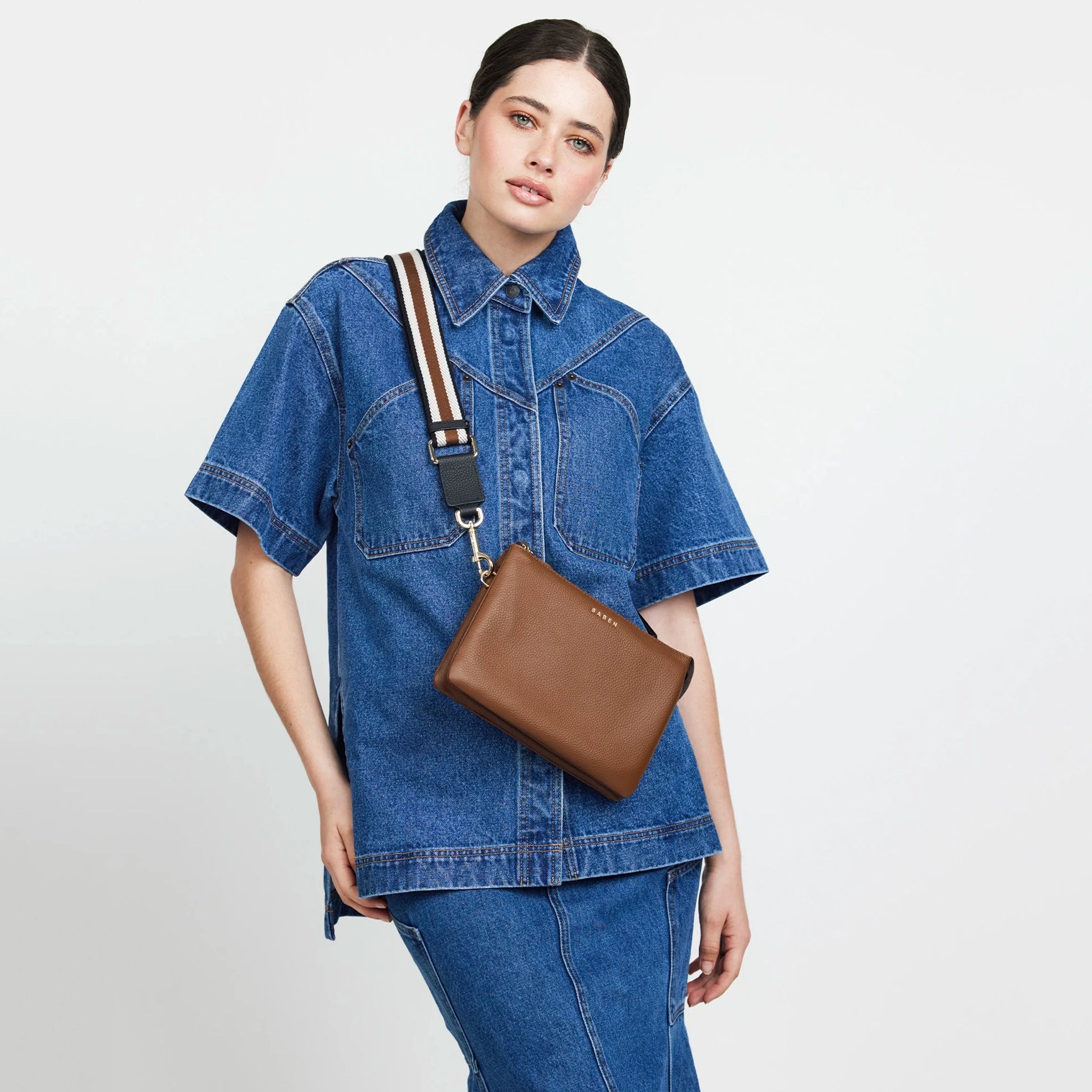 Woman wearing a denim outfit with a brown bag on a light gray background